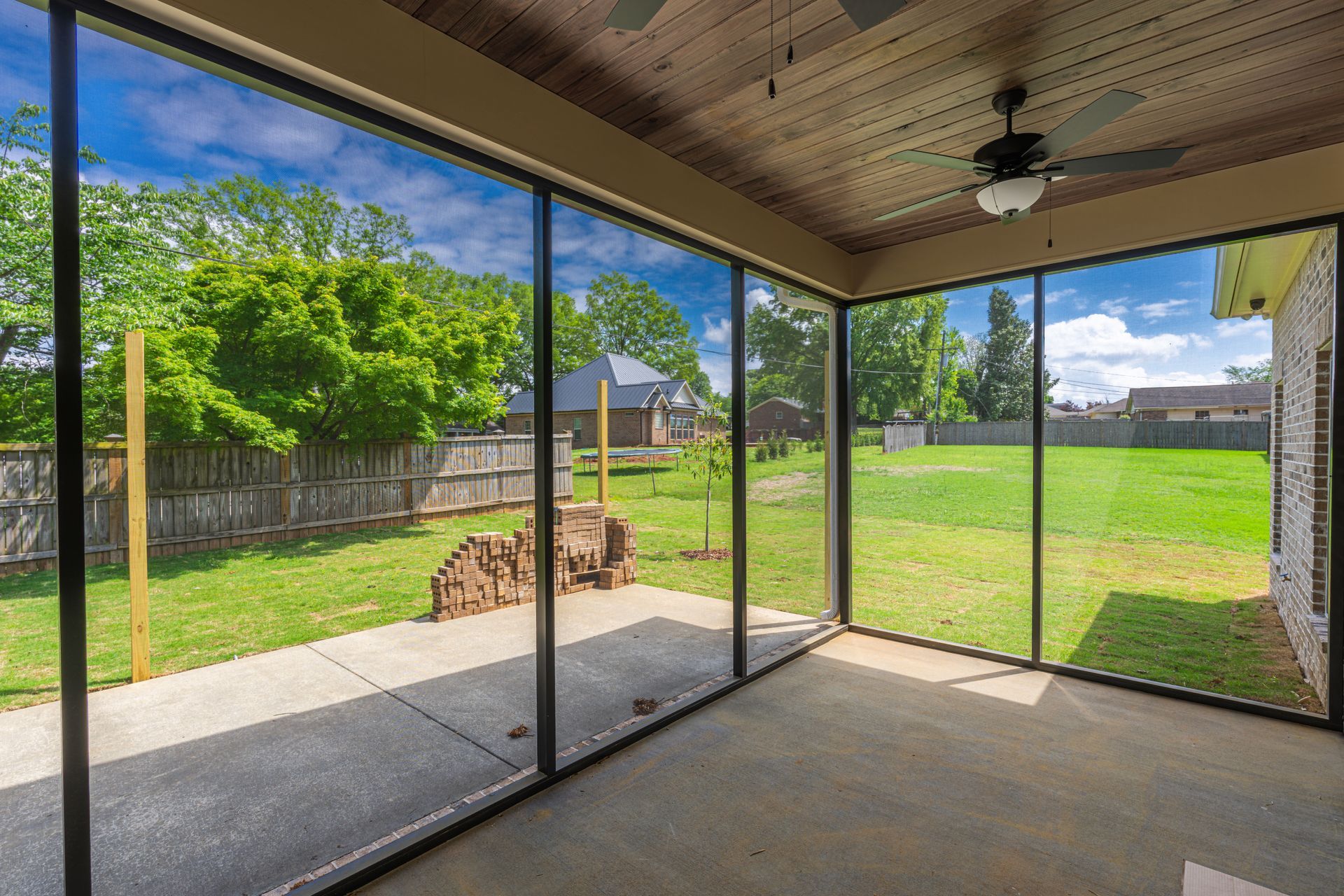 Screened patio overlooking a grassy backyard with trees and a fence