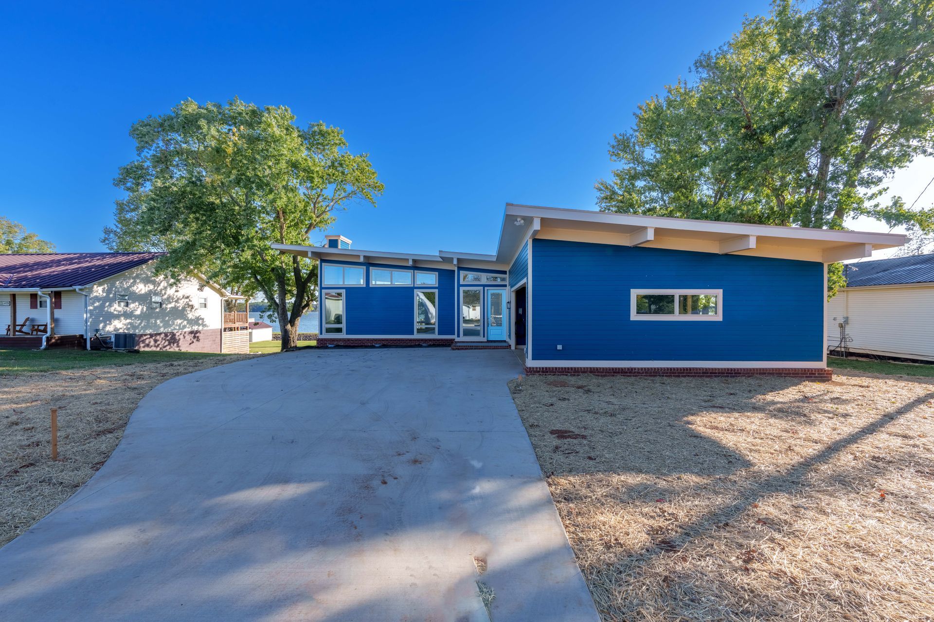 Blue single-story house with a wide driveway, front steps, and trees under a clear sky