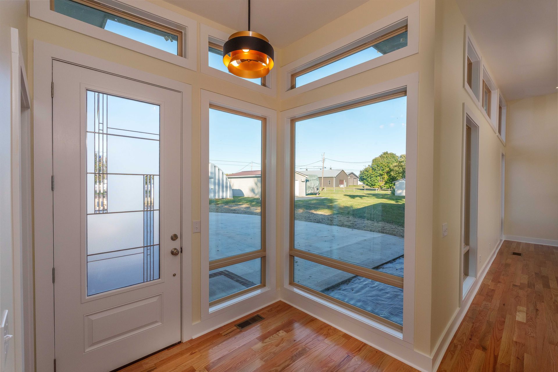 Bright entryway with white double doors, glass windows, warm pendant light, and hardwood floors overlooking a yard.