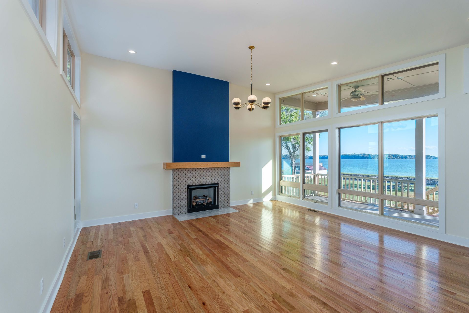 Bright empty living room with hardwood floors, fireplace, and large windows overlooking water