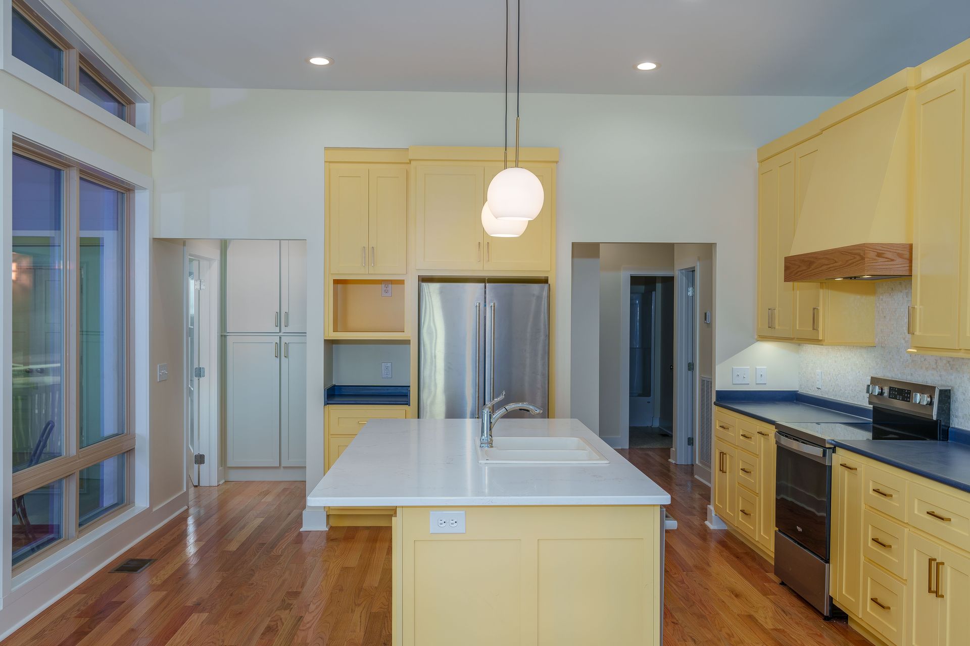 Bright kitchen with wood floors, pale cabinets, stainless steel appliances, and a central island under pendant lights