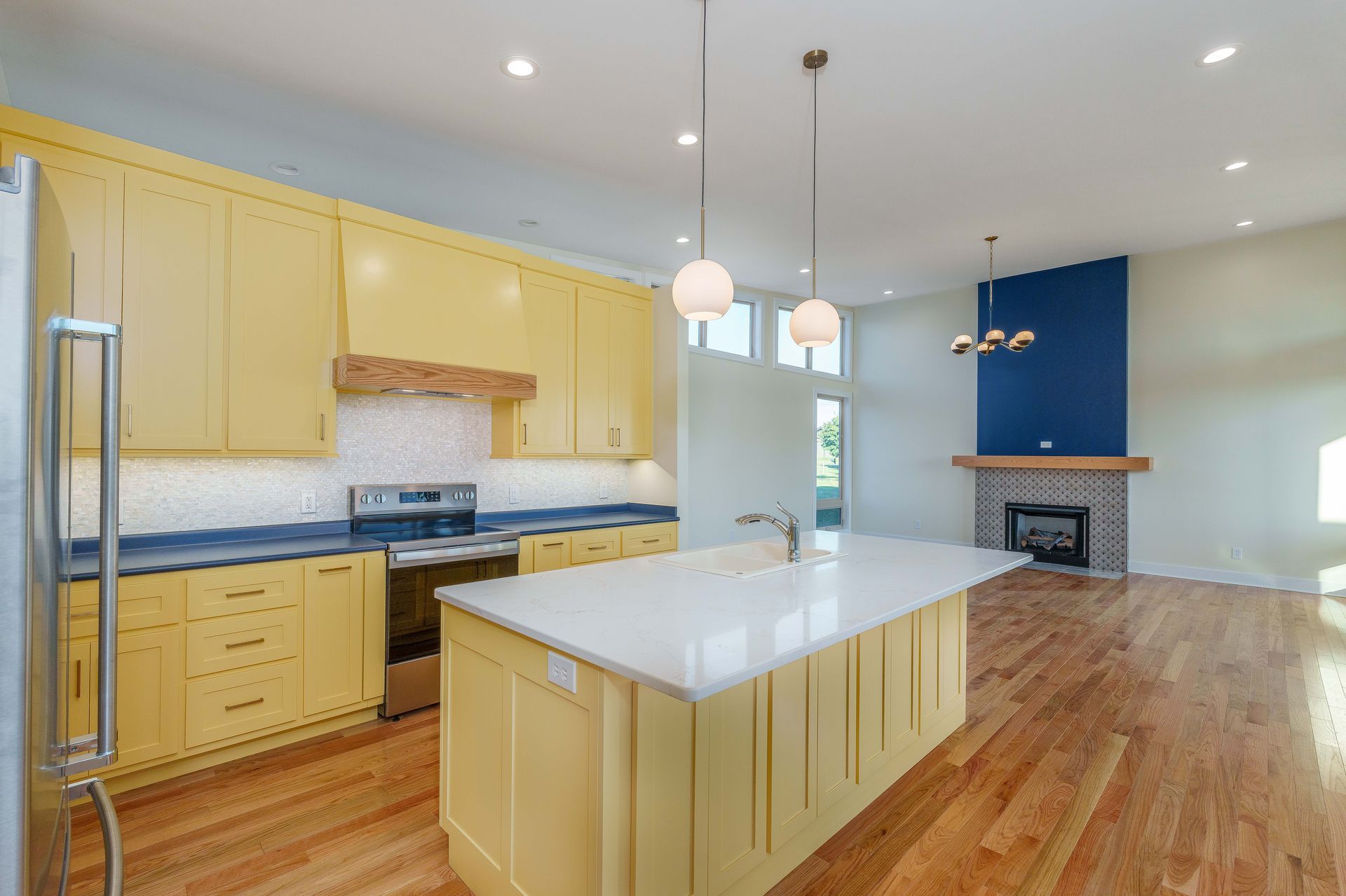 Bright modern kitchen with yellow cabinets, island, hardwood floors, and blue accent wall by a fireplace