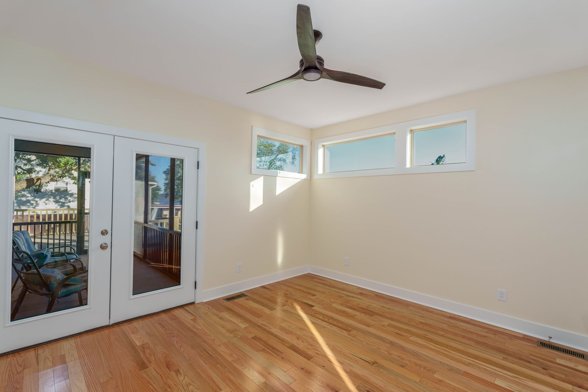 Empty bright room with hardwood floors, French doors, narrow windows, and a ceiling fan