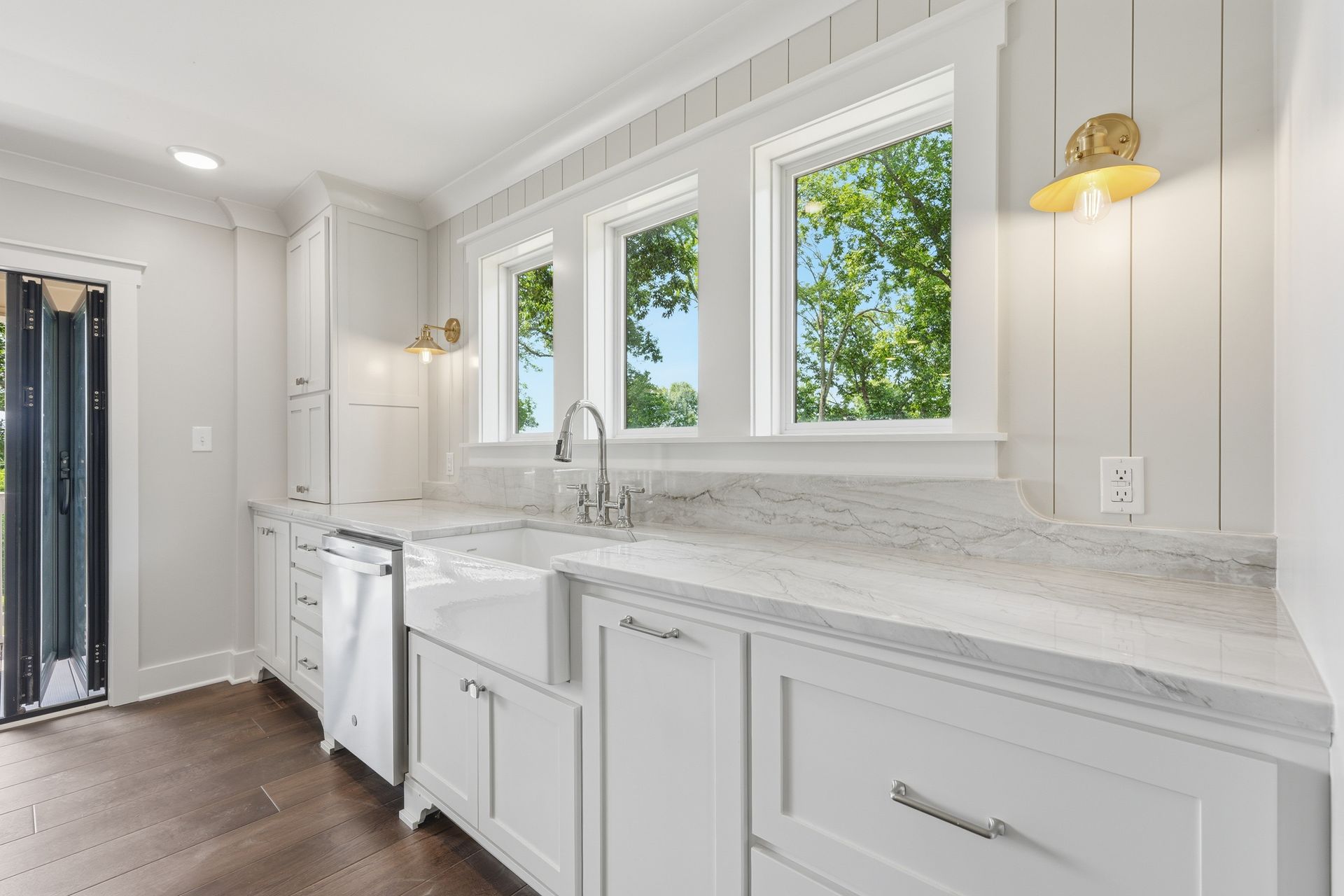 Bright white laundry room with cabinets, countertop, sink, and three windows overlooking greenery