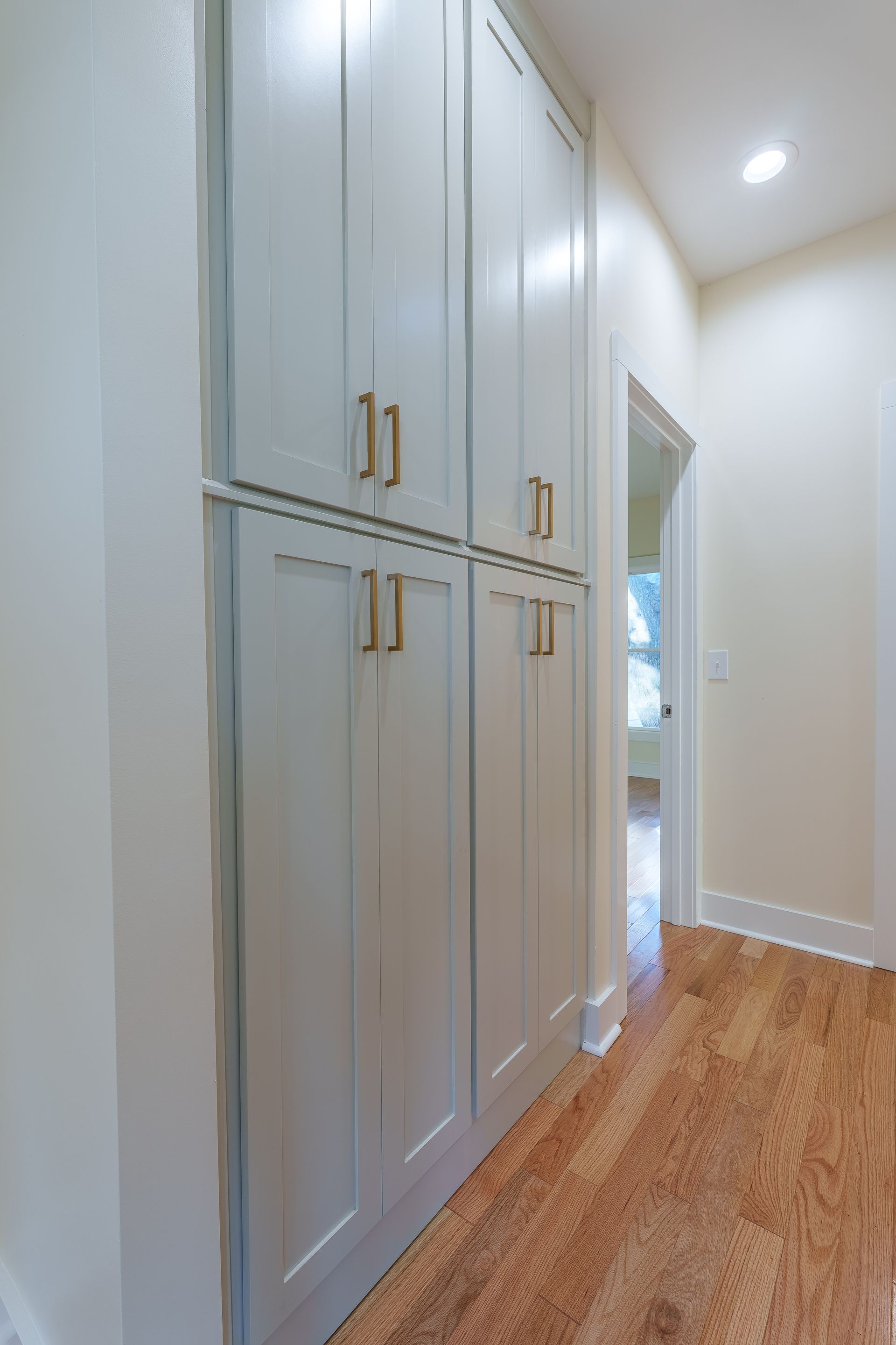 Built-in light gray cabinets in a bright hallway with hardwood floors and a doorway.