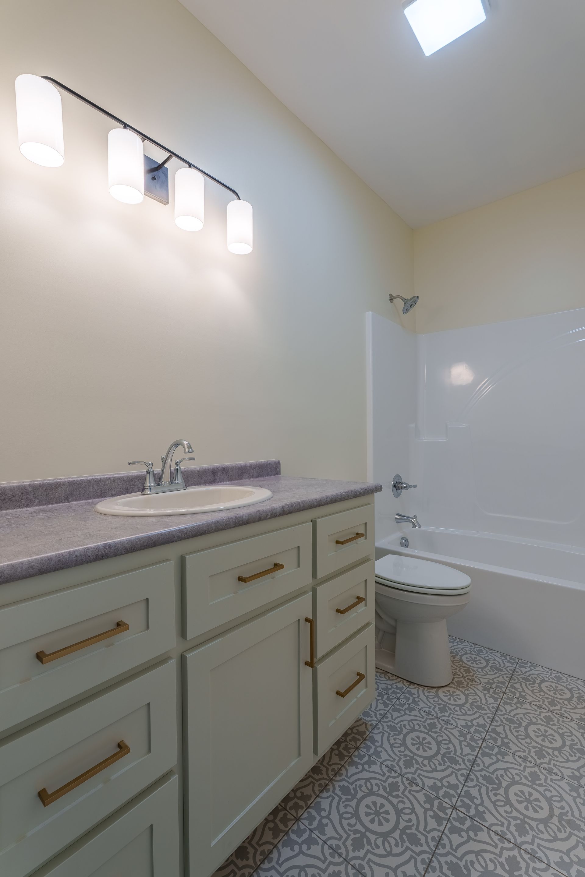 Bright bathroom with vanity, mirror lights, toilet, tub, and patterned tile floor.