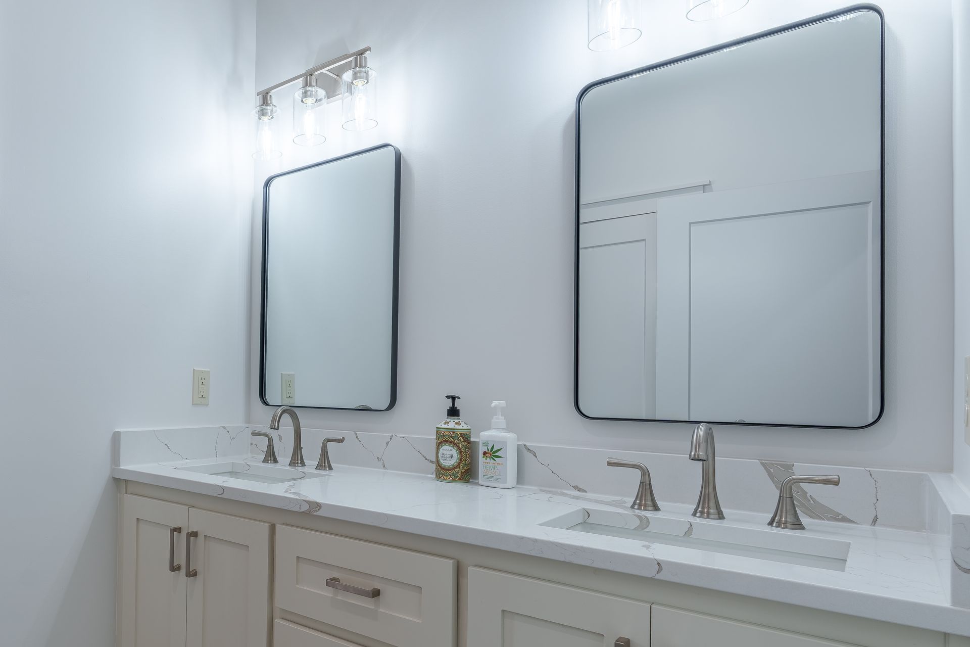 Bright white bathroom vanity with two mirrors, dual faucets, and marble countertop with toiletries