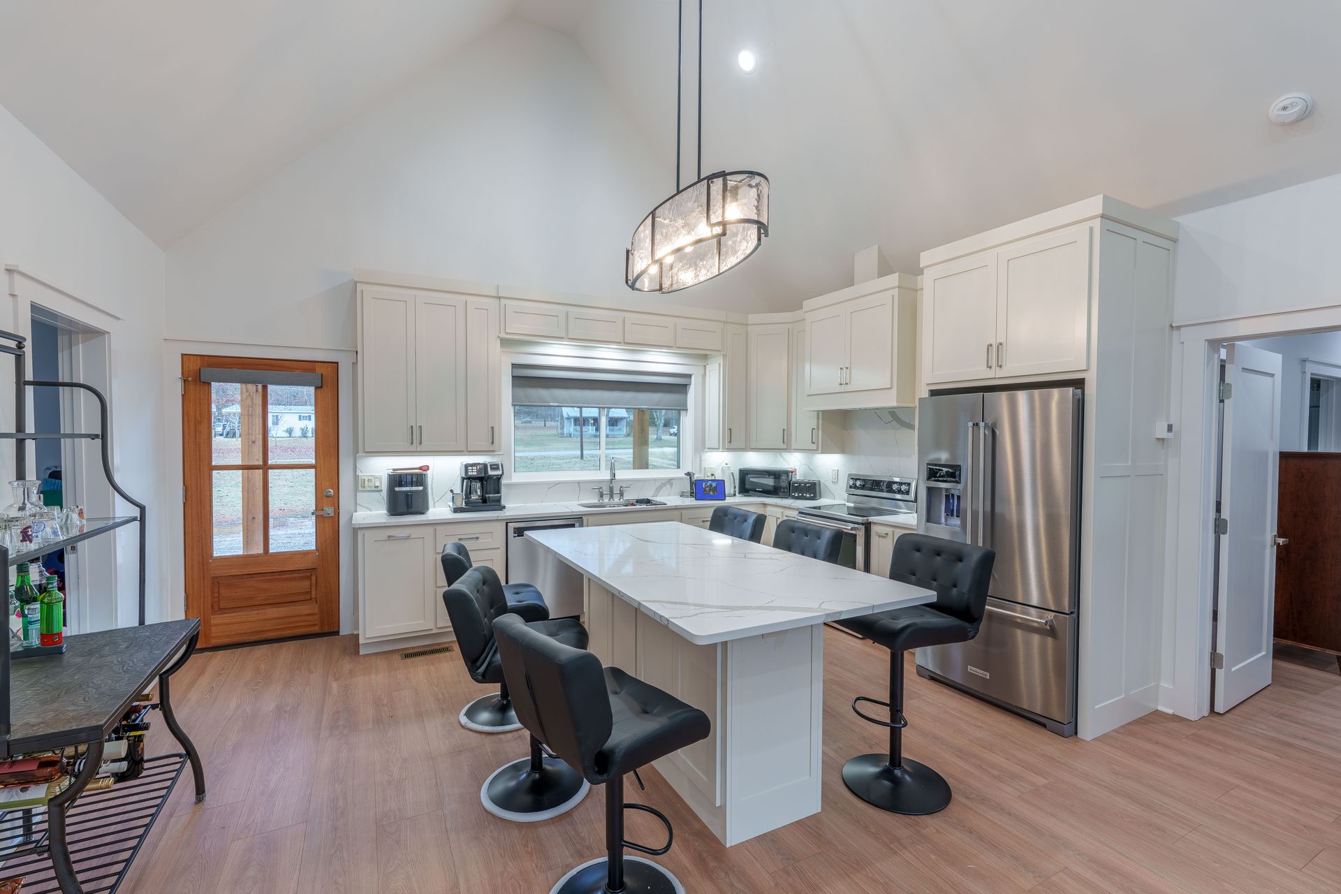 Modern white kitchen with island, bar stools, stainless fridge, and skylight under vaulted ceiling