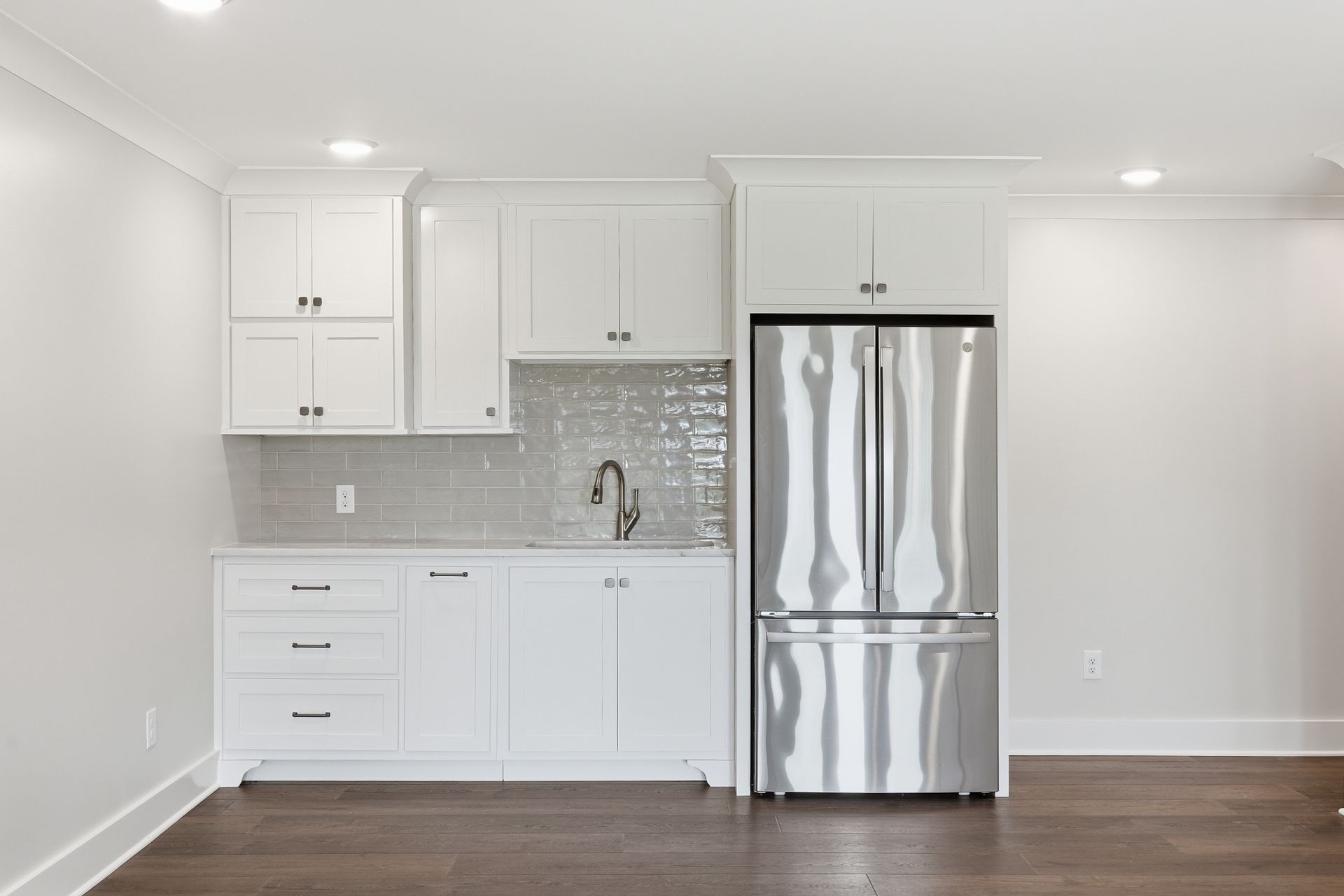 Bright white kitchen with stainless steel refrigerator, white cabinets, and wood floor