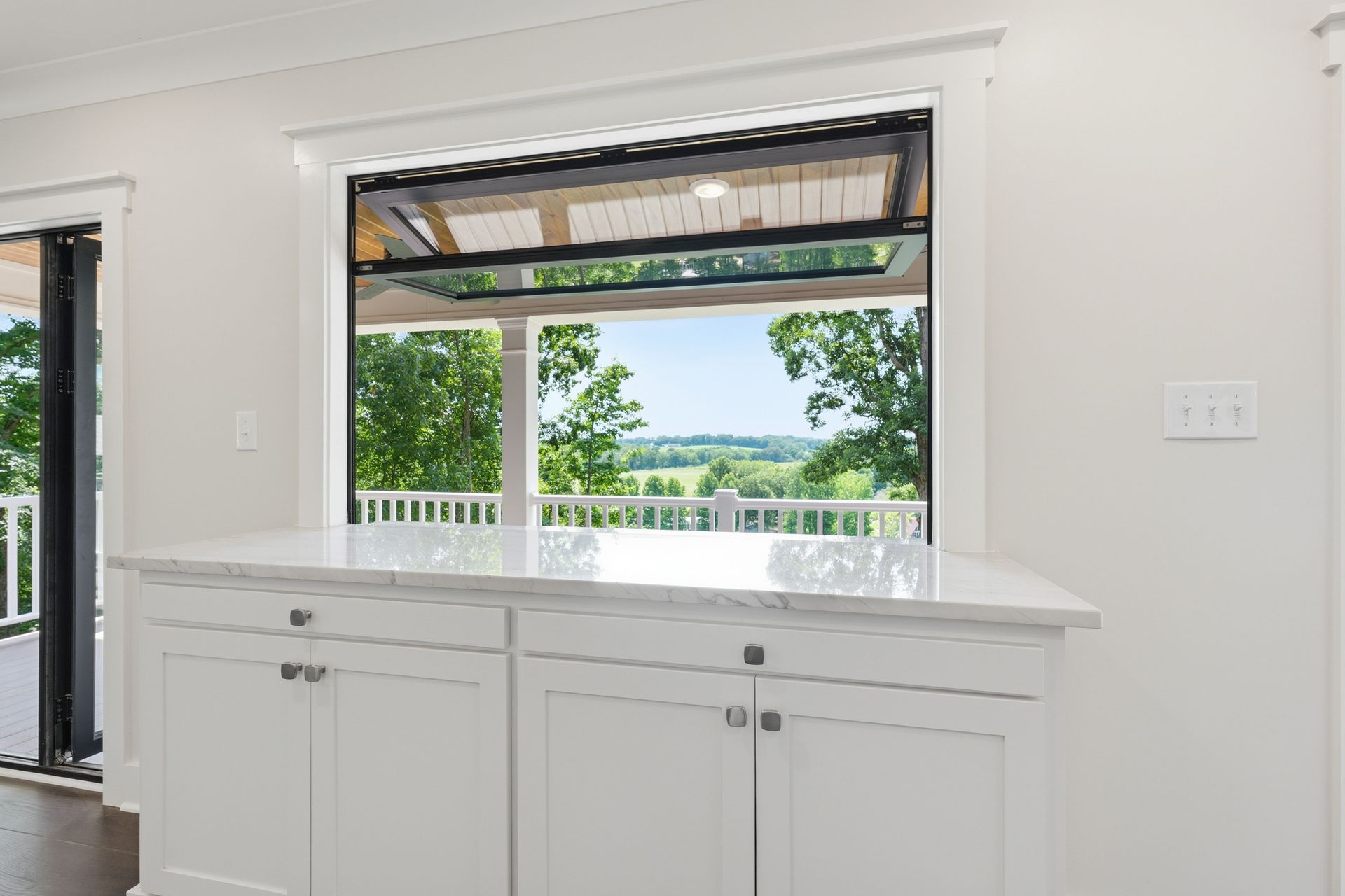 Bright white kitchen with a wide window overlooking greenery and water.
