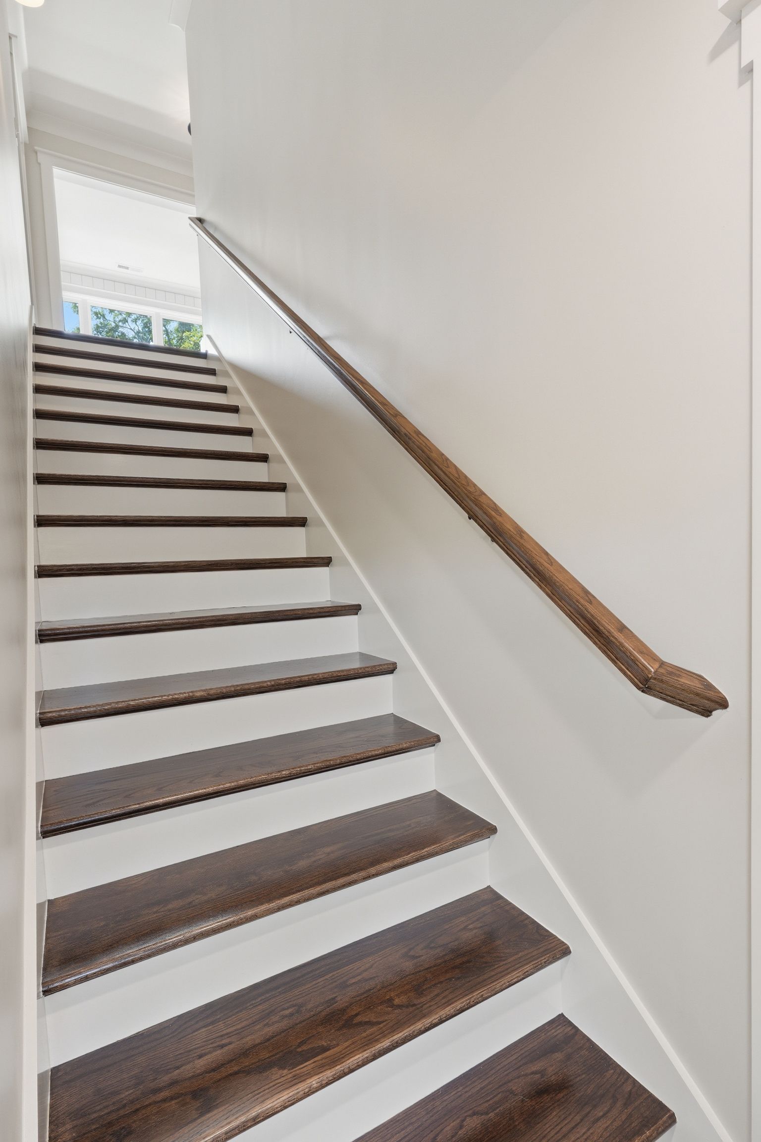 Staircase with white walls, dark wooden steps, and a wooden handrail