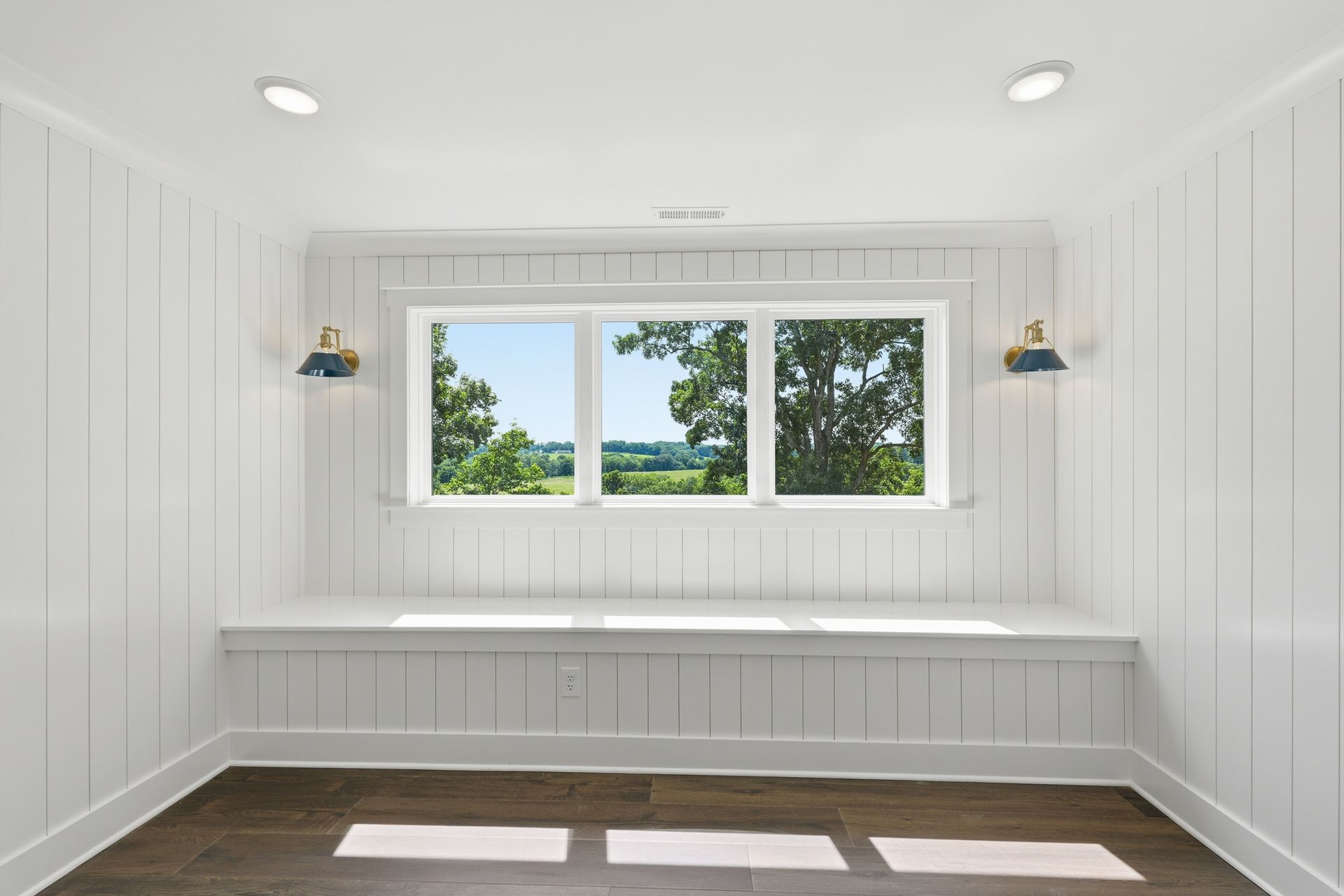 Bright white built-in bench nook with window seat and three-pane window overlooking trees