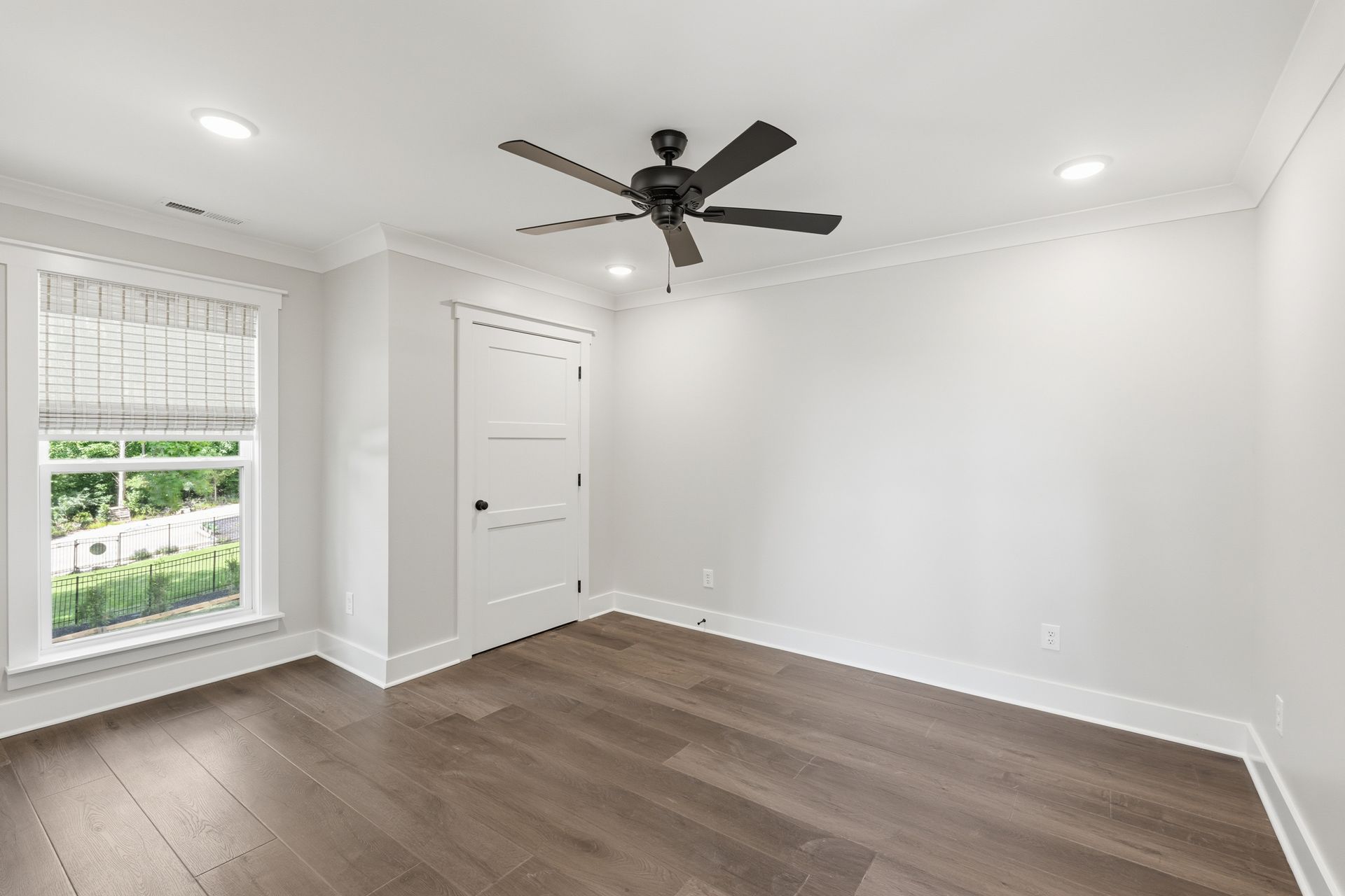 Empty white bedroom with hardwood floors, a ceiling fan, and a window with blinds