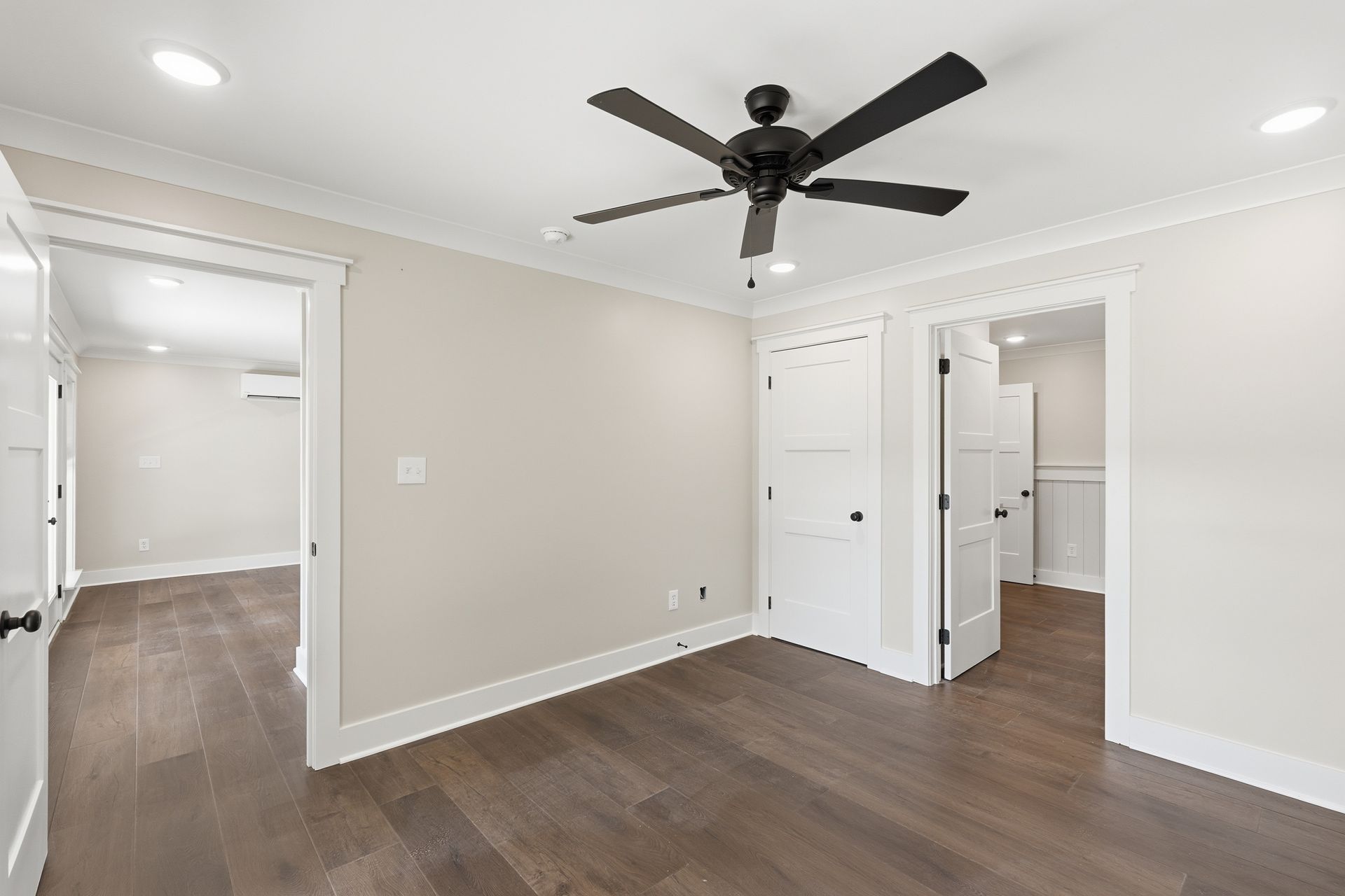 Empty modern bedroom with dark wood floors, white walls, ceiling fan, and an open closet door