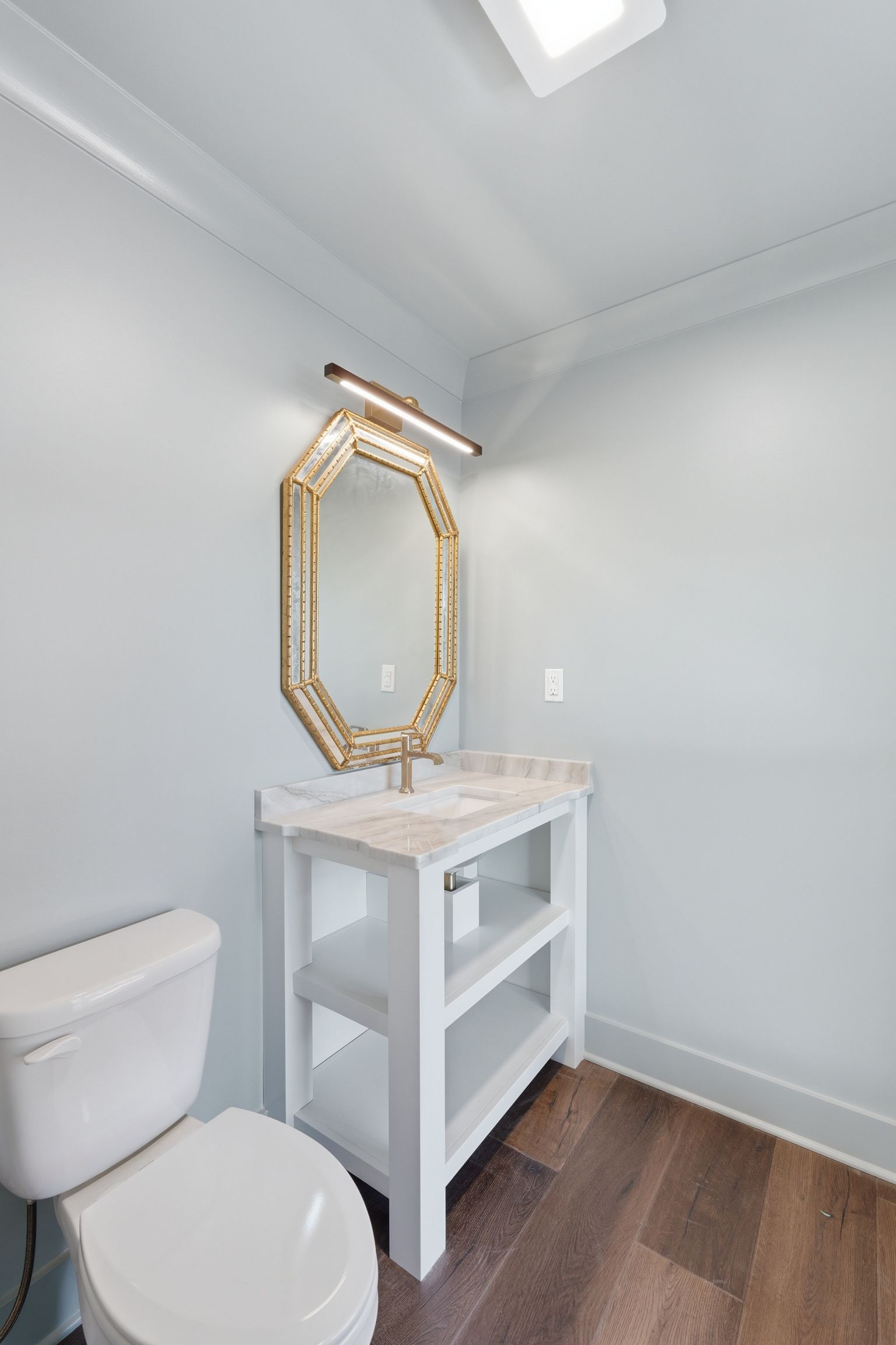 Small bathroom corner with white vanity, ornate mirror, toilet, and wood-look floor.