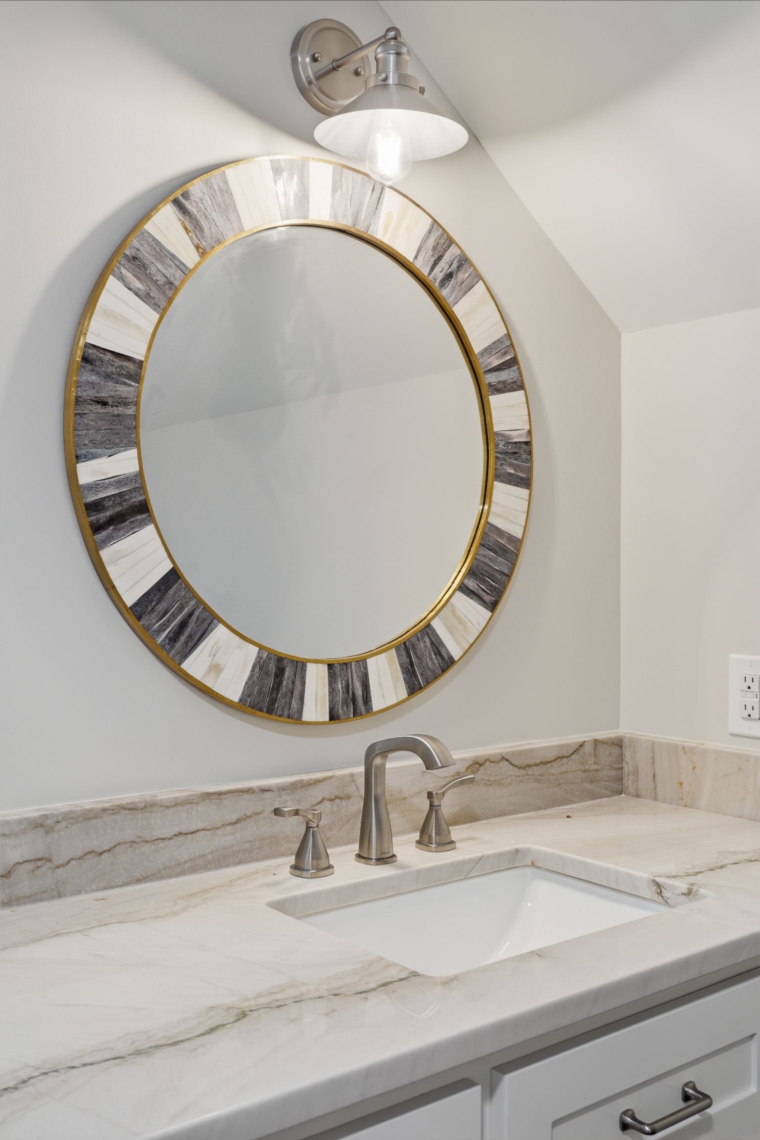 Bathroom vanity with round gold-framed mirror, white sink, chrome faucet, and marble countertop
