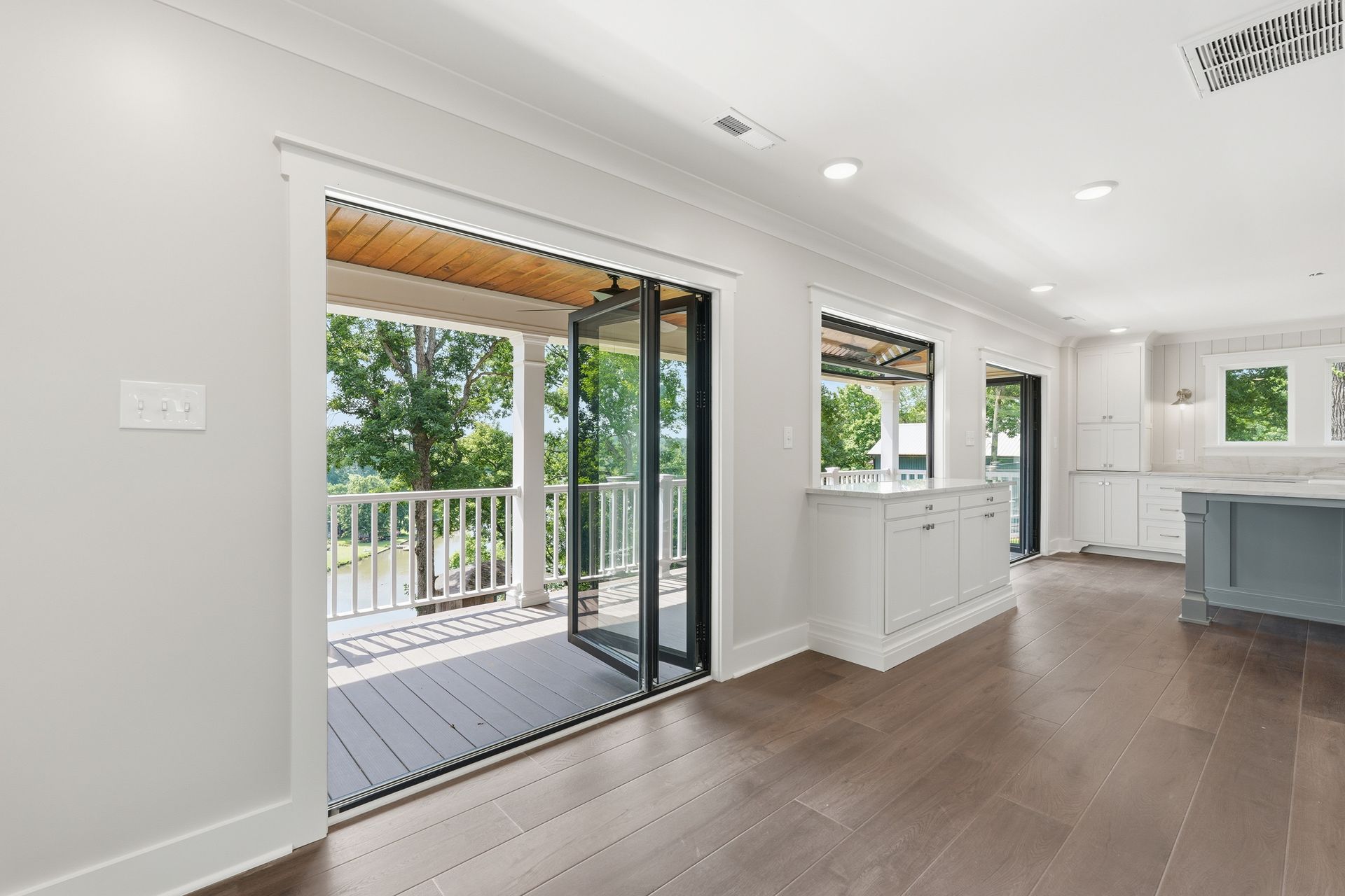 Bright open living room with wood floors and sliding doors to a covered deck and trees outside