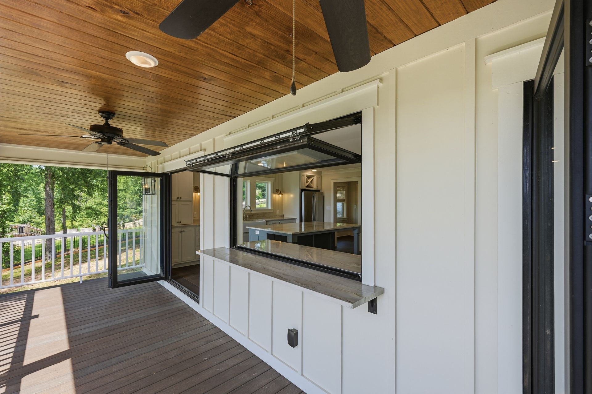 Covered porch with wood ceiling, black ceiling fans, and a white outdoor serving window open to a kitchen
