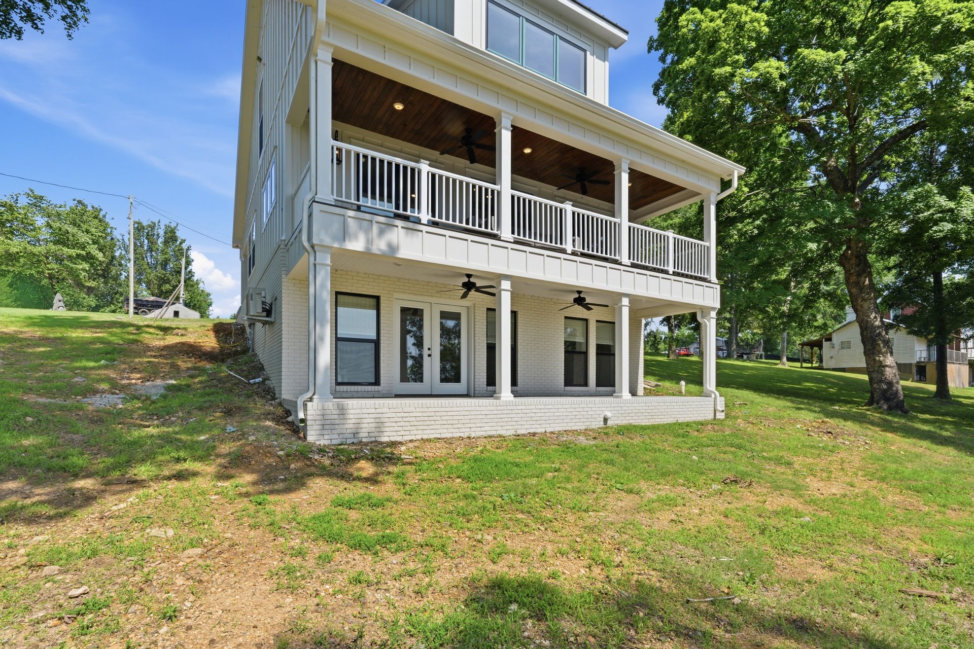Two-story white house with front porch and balcony on a grassy hillside