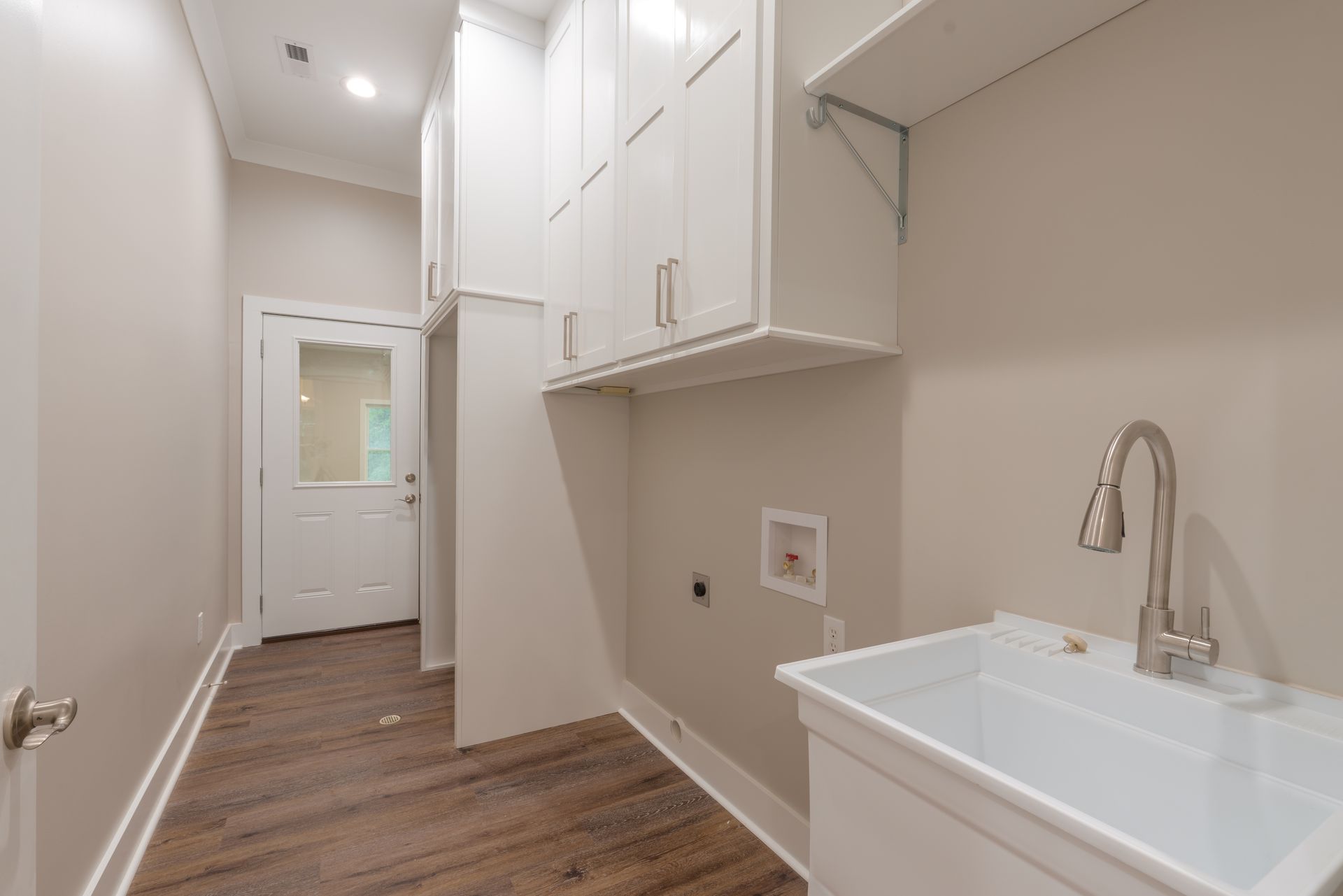 Narrow laundry room with white cabinets, utility sink, and wood-look flooring