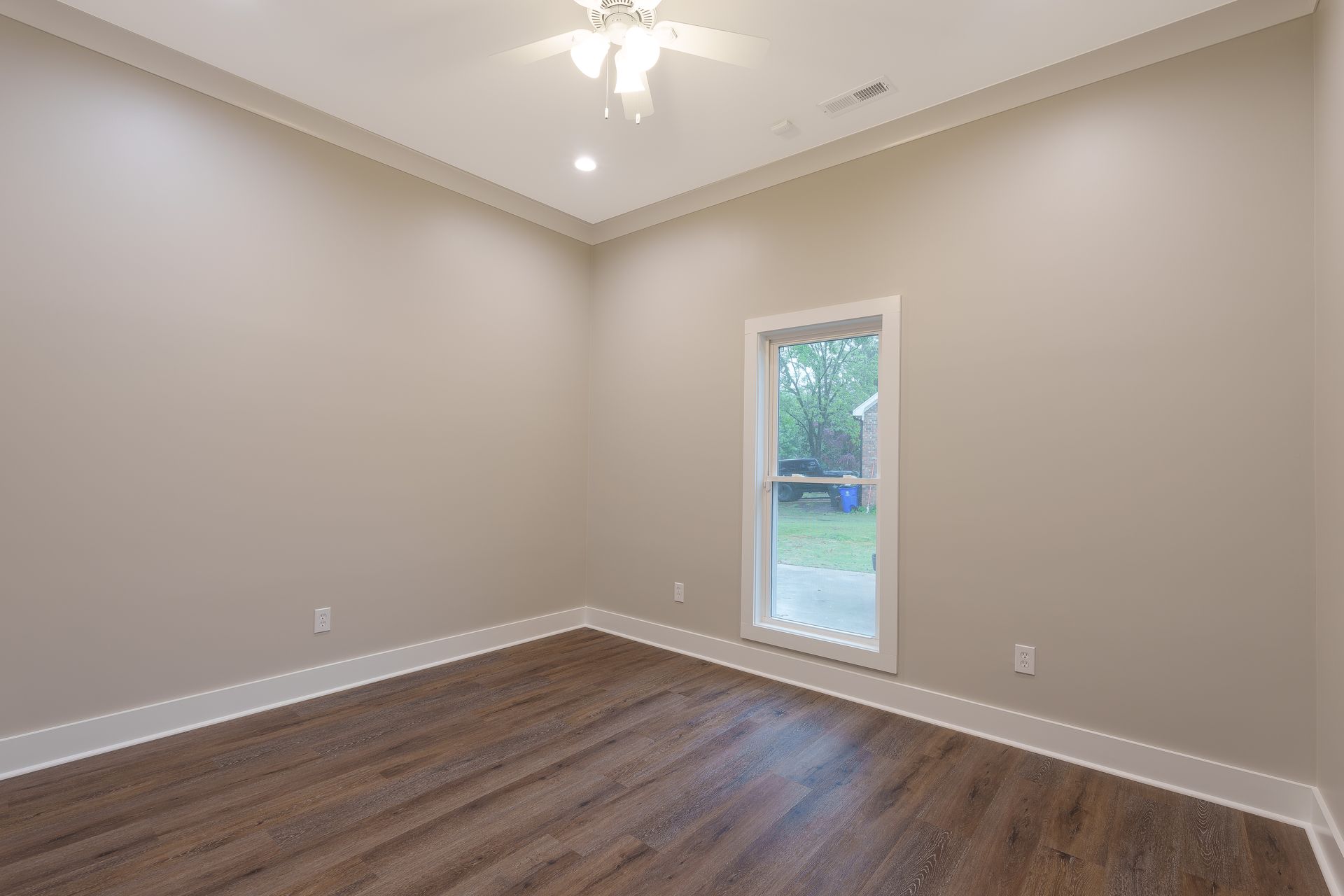 Empty beige room with wood floors and a small window showing greenery outside.