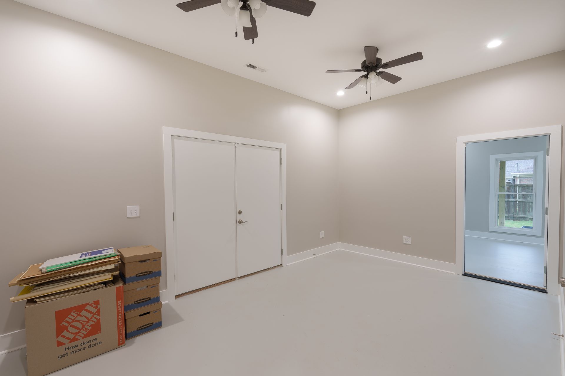 Empty beige room with white double doors, ceiling fan, and boxes stacked in the corner