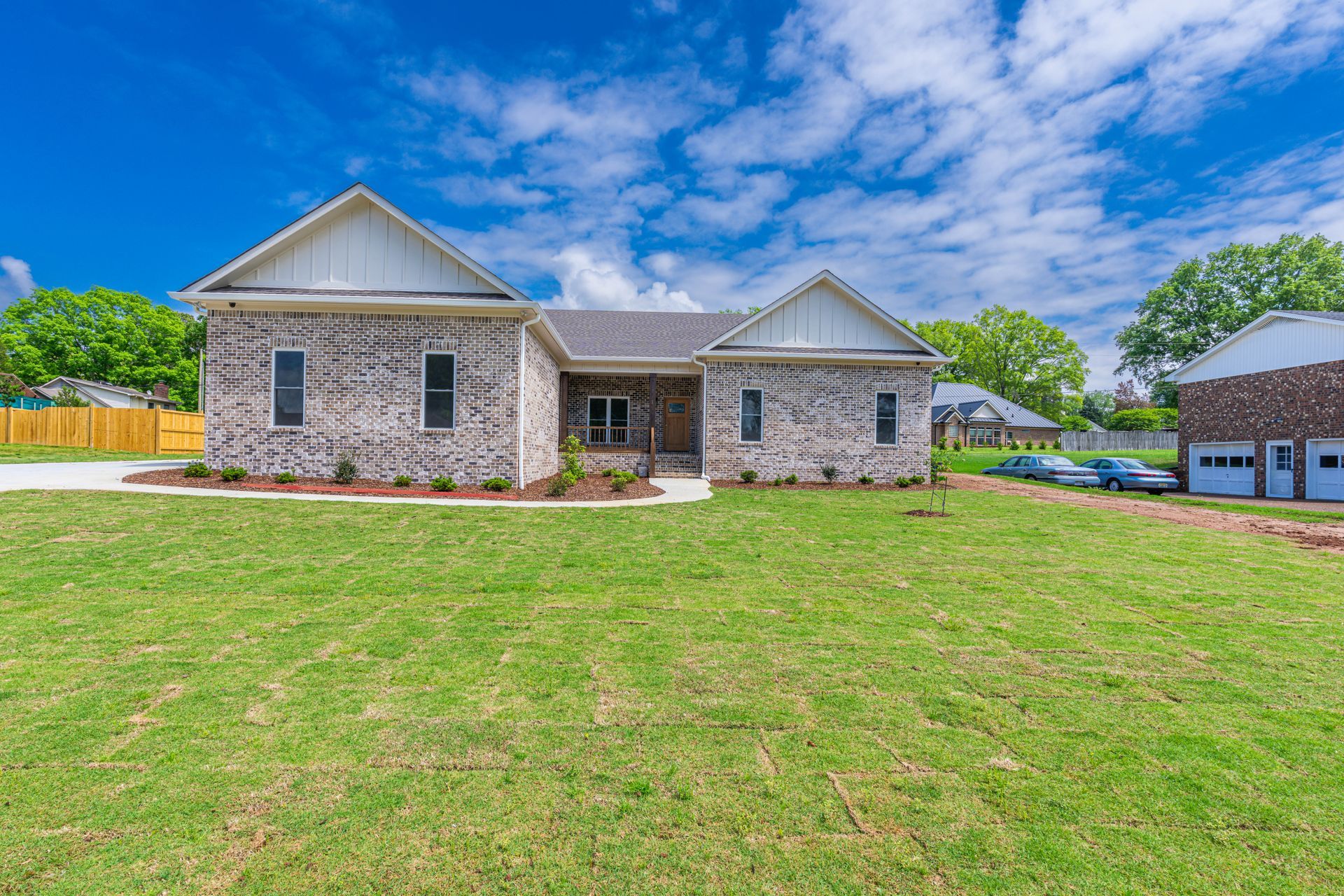 Stone suburban house with a large green lawn under a bright blue sky