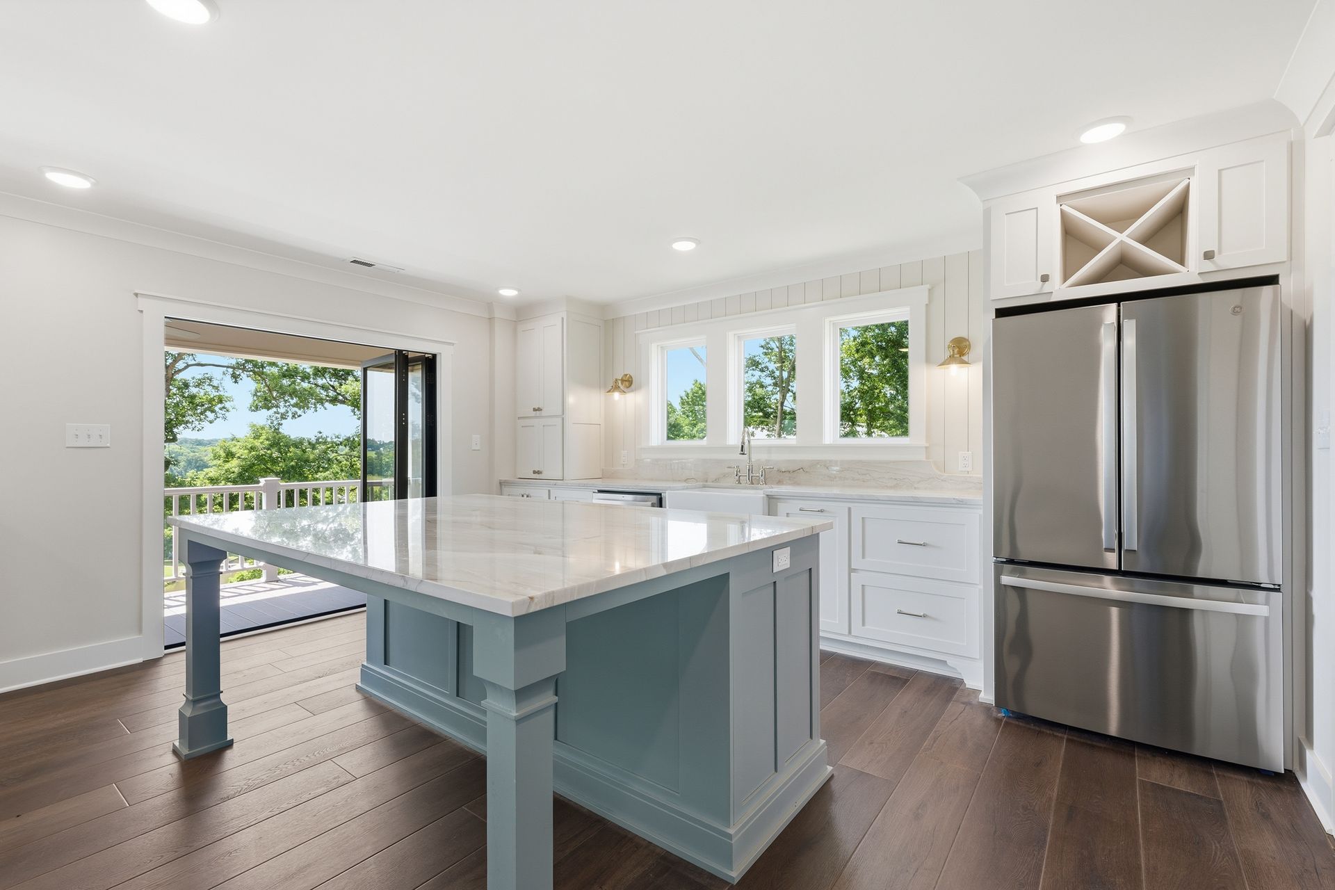 Bright modern kitchen with marble island, stainless steel fridge, white cabinets, and dark wood floors
