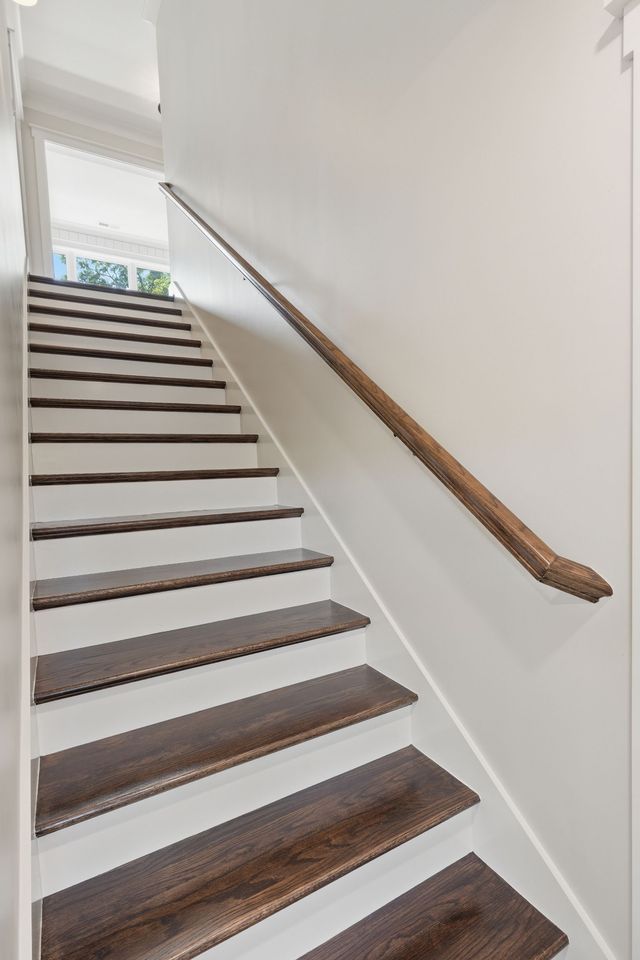 Staircase with white walls, dark wooden steps, and a wooden handrail in a bright hallway