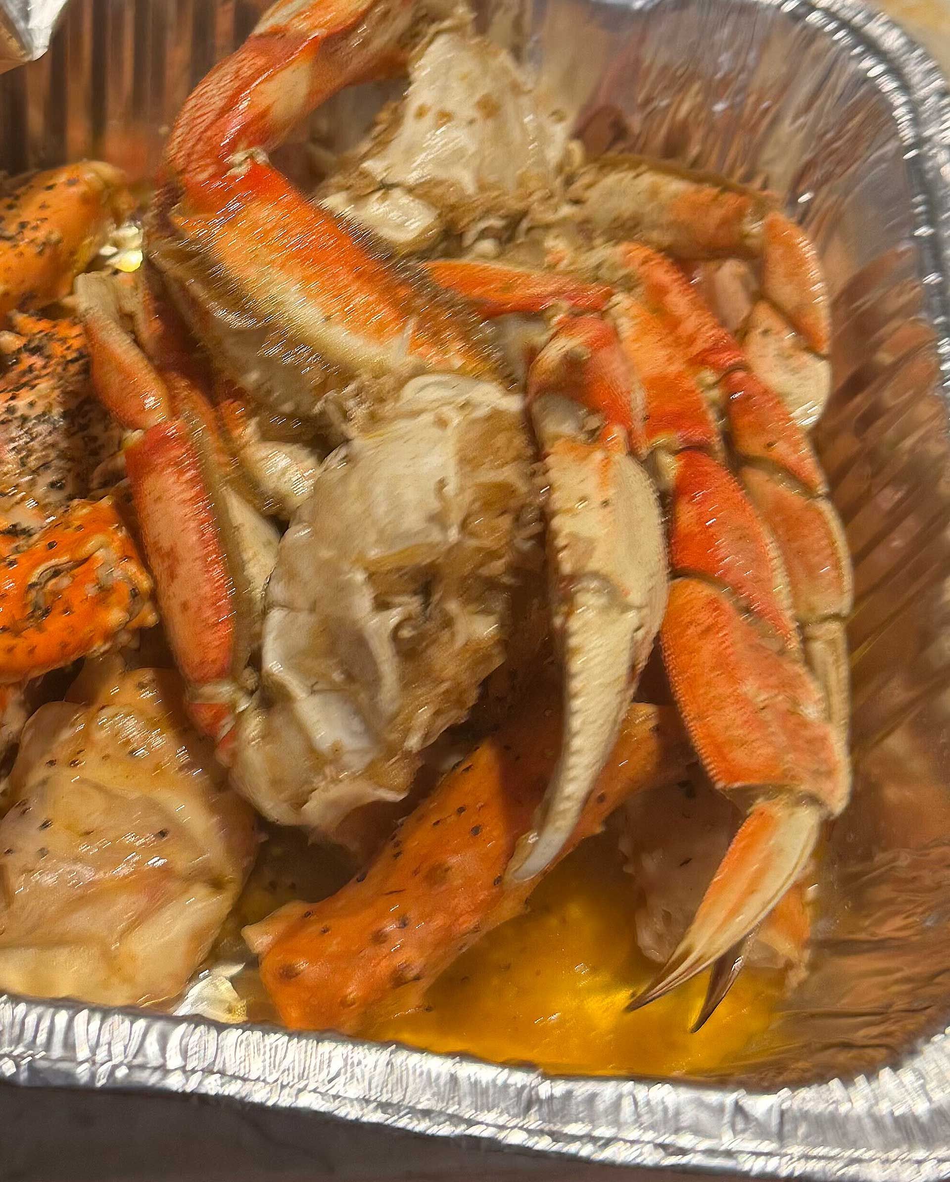 A close up of Cajun crab legs in a tin foil container