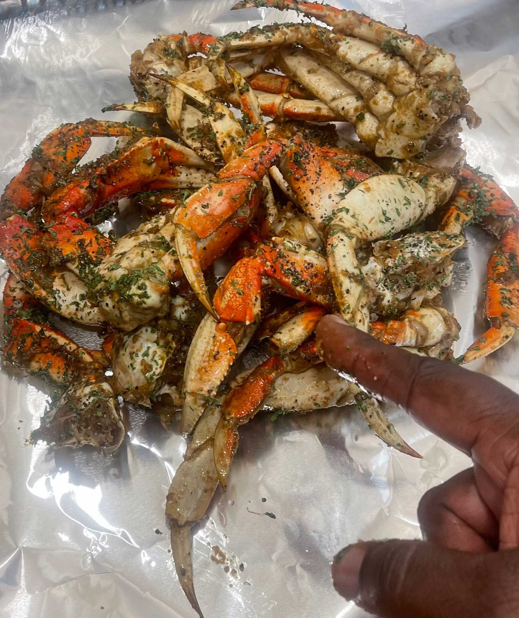 A person is pointing at a pile of Cajun crabs on foil.