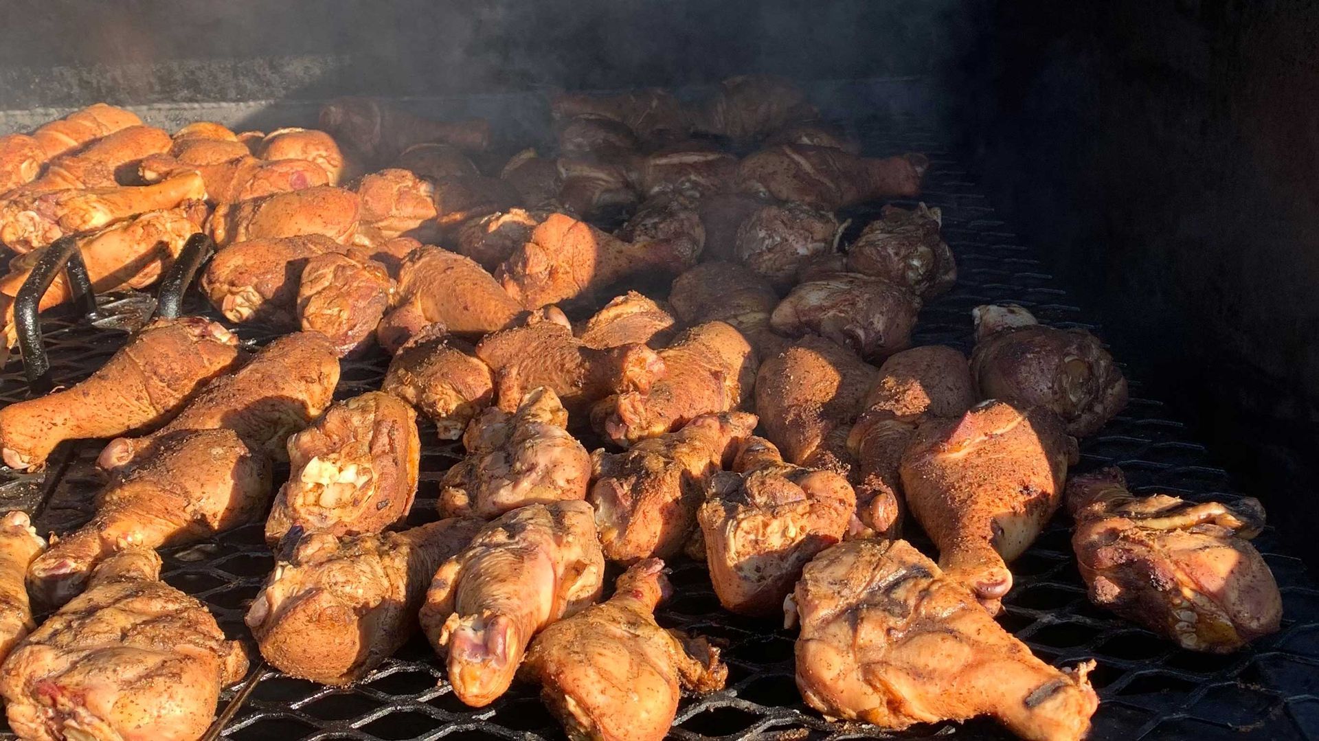 A bunch of meat is cooking on a grill with smoke coming out of it