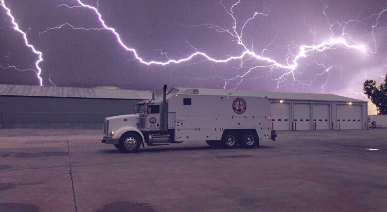 White truck with lightning flashing in a stormy sky near a building.