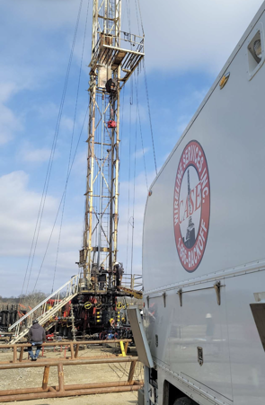 Oil rig with white service truck featuring a logo, on a bright, sunny day.
