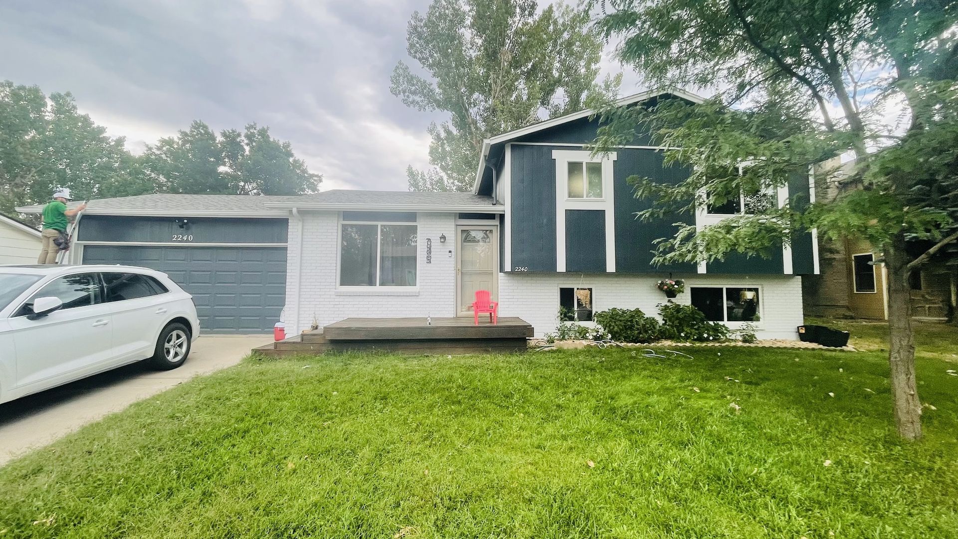 White house with dark blue accents, a garage, and a green lawn under an overcast sky.