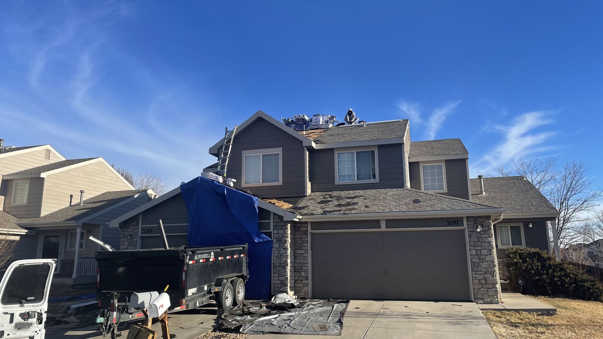 House with roof partially removed, blue tarp, workers on roof, blue sky.
