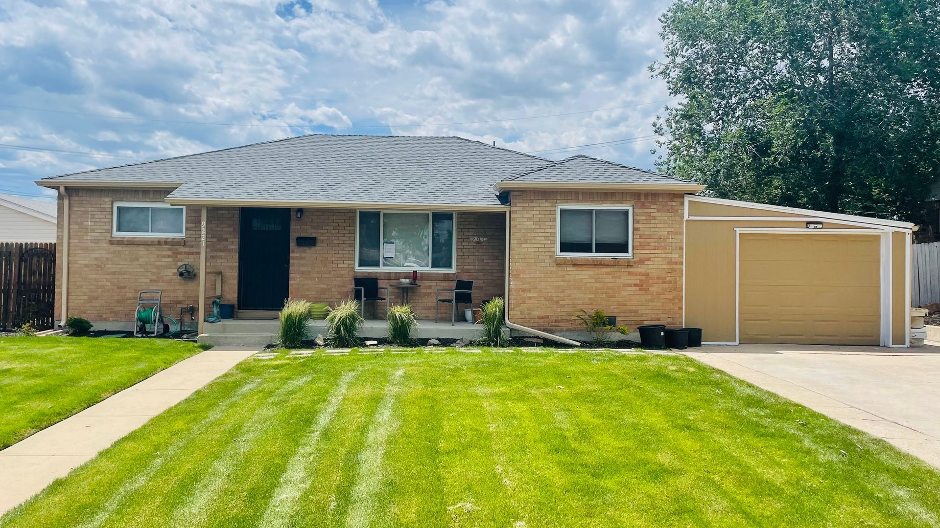Brick house with green lawn, sidewalk, and attached tan garage under a cloudy sky.