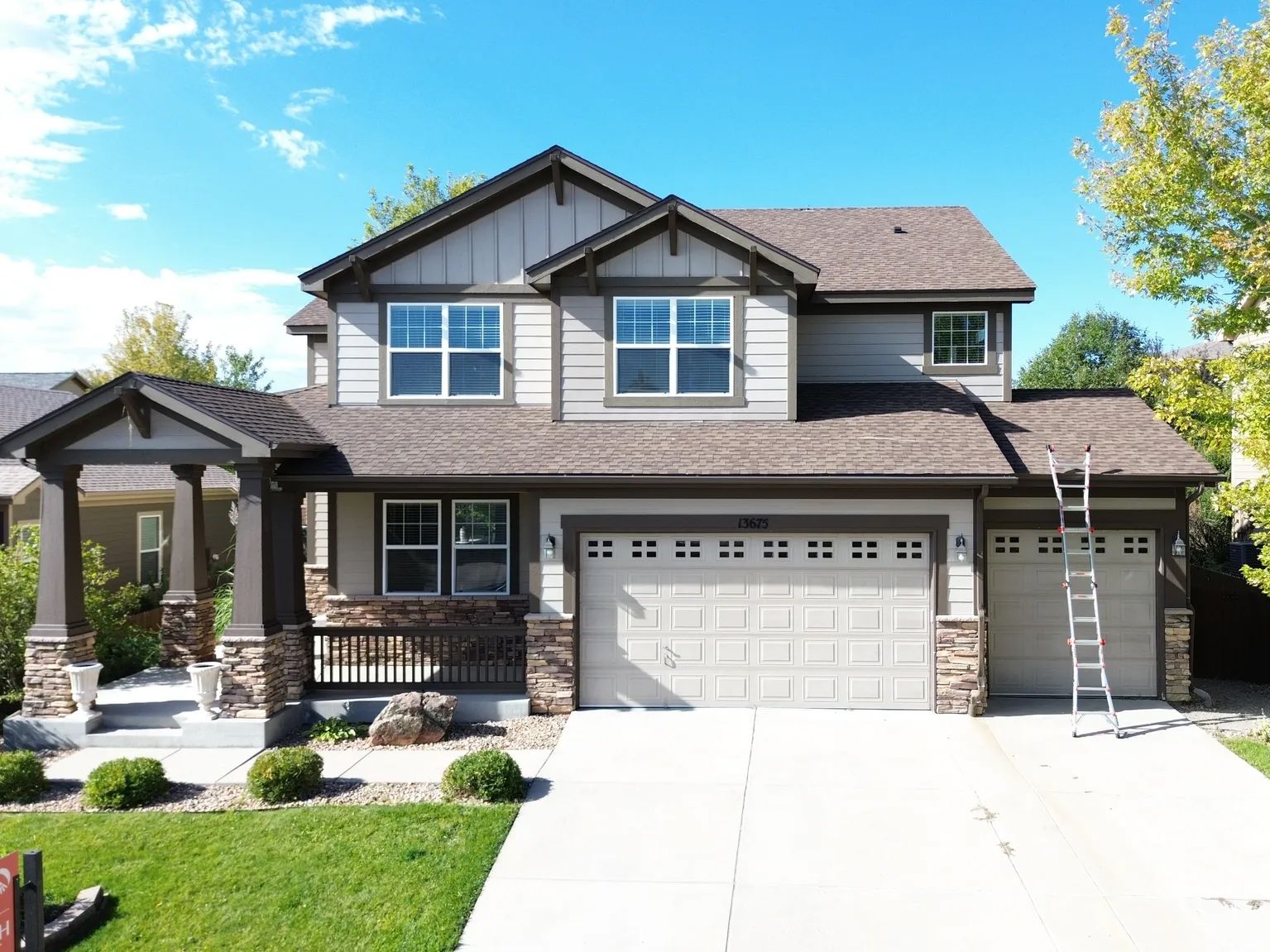 Two-story house with tan siding, a gray roof, and a two-car garage on a sunny day.