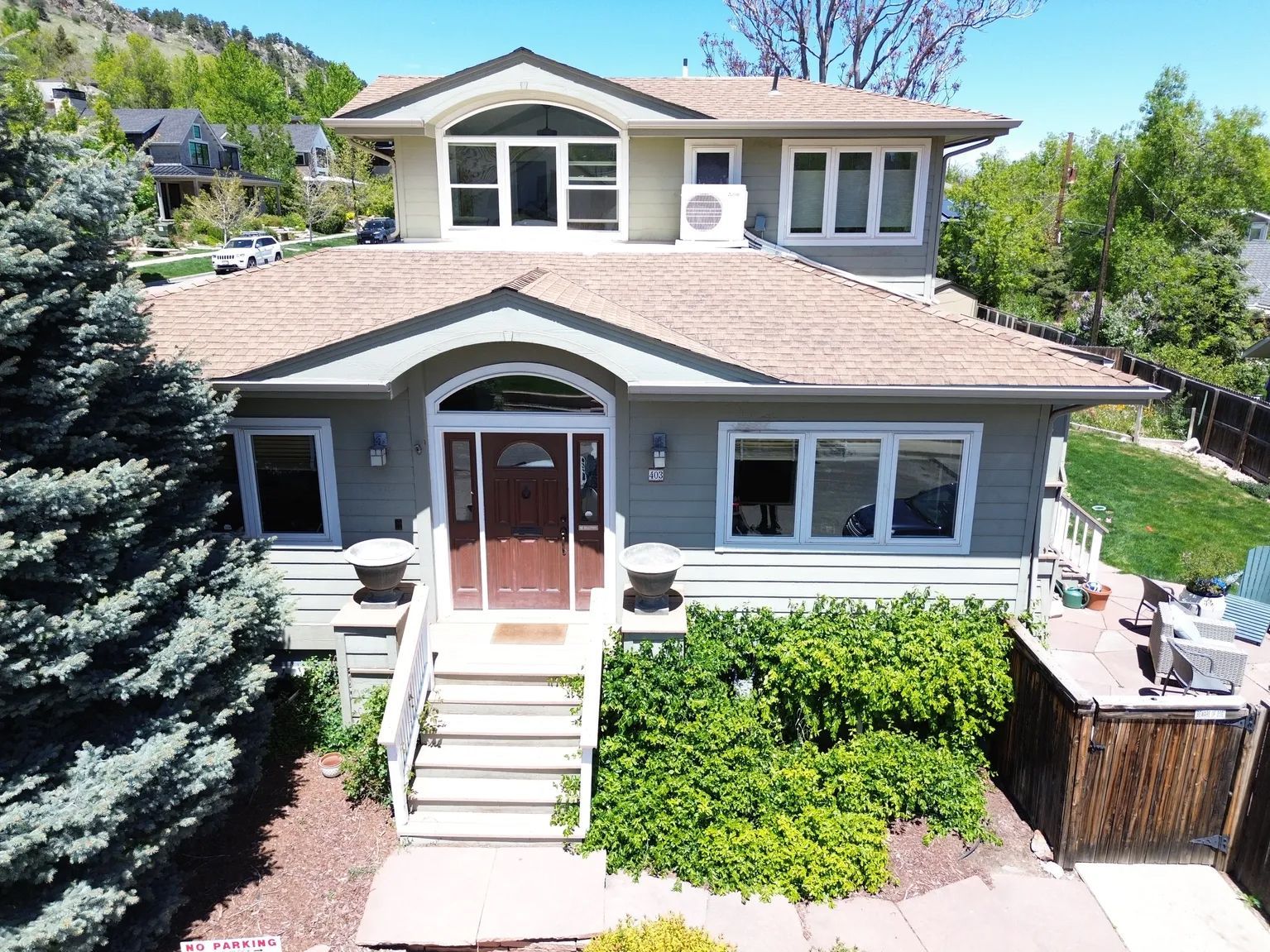 Two-story house with light green siding and brown trim, small front yard, trees, and stairs leading to the entrance.