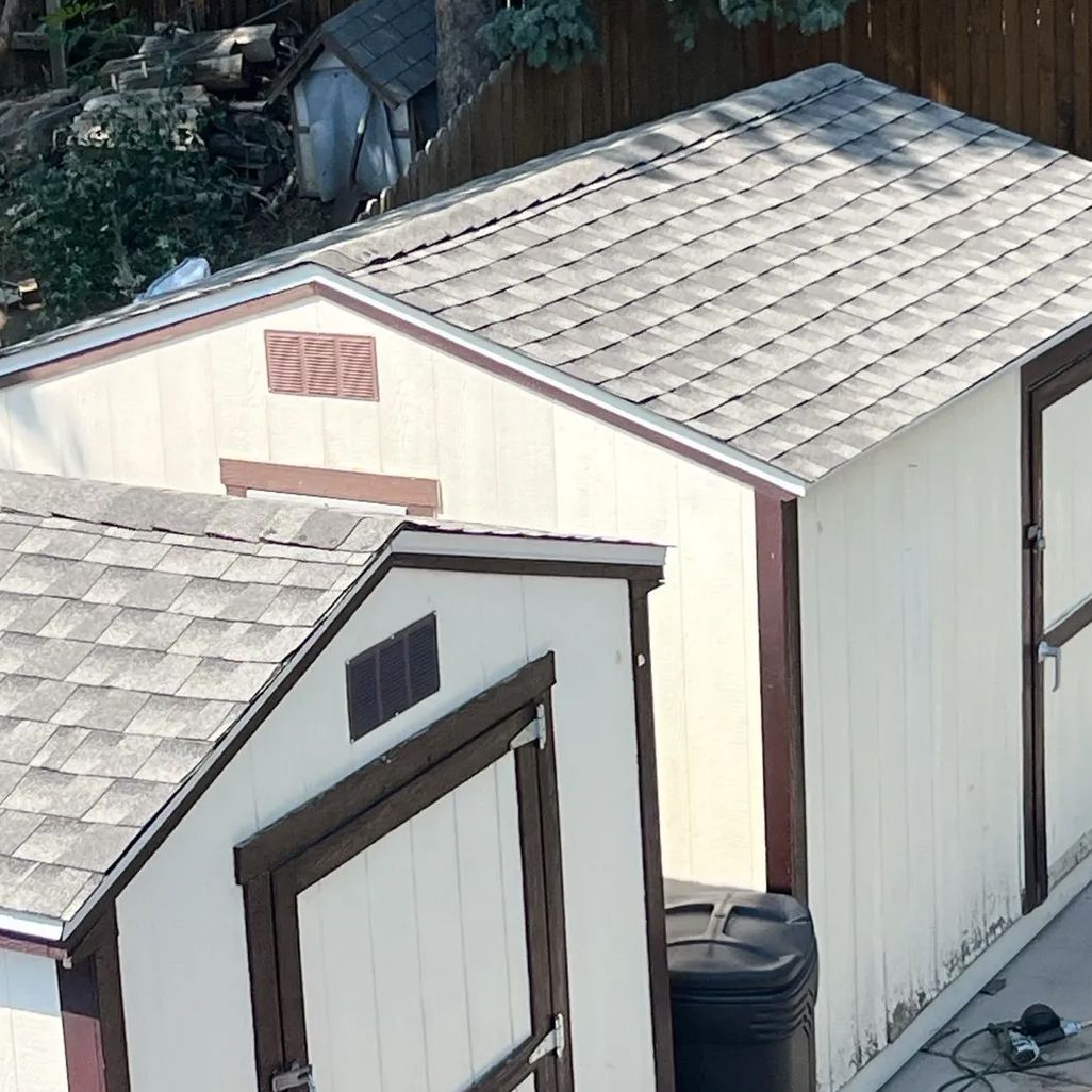 Two sheds with shingle roofs and brown trim. Beige siding. One has a small vent.