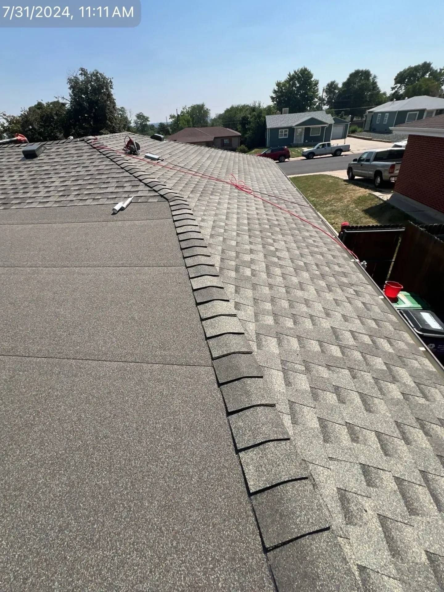 Roof shingles being installed on a house, sunny day, residential neighborhood.