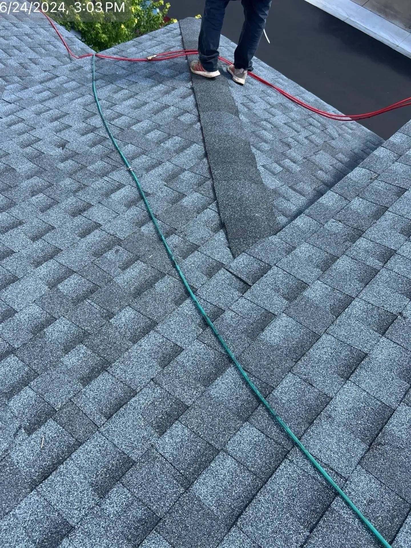Person on roof inspecting shingles; blue jeans, gray shingles, green and red rope.