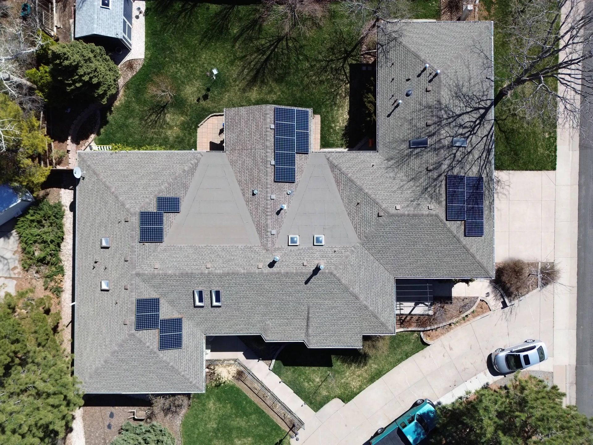 Roofer in safety gear, kneeling on a rooftop, using a power tool against a blue sky.