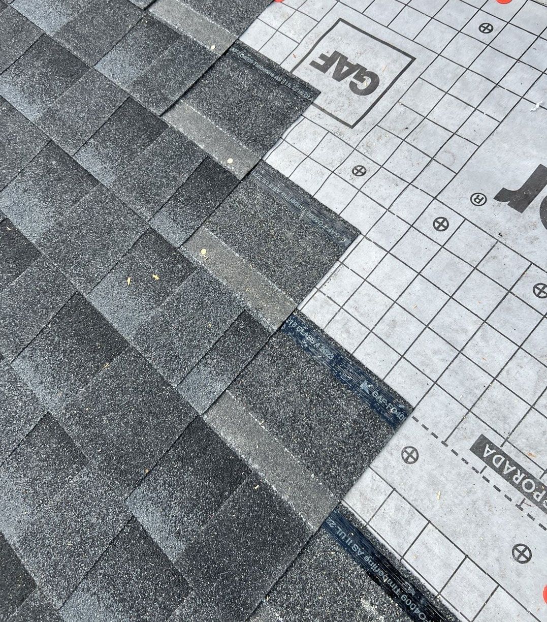 Close-up of asphalt shingles partially covering a roof. The right side shows roofing underlayment.