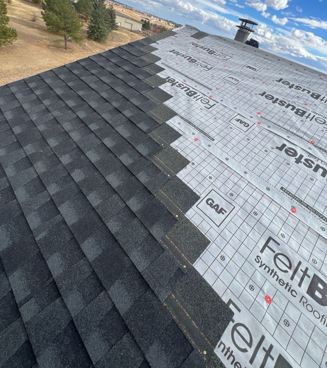 Roof with asphalt shingles being installed over synthetic underlayment; blue sky.