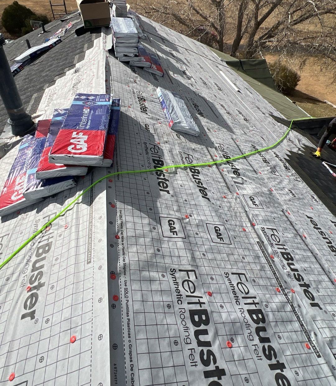 Roofing work in progress:  Underlayment and shingle bundles on roof. Bright sunshine.