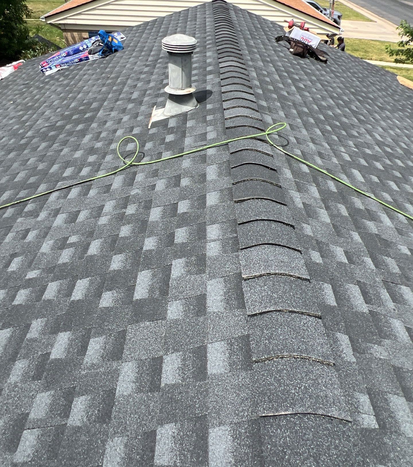 A newly shingled roof with a vent and a safety rope, outdoors in daylight.