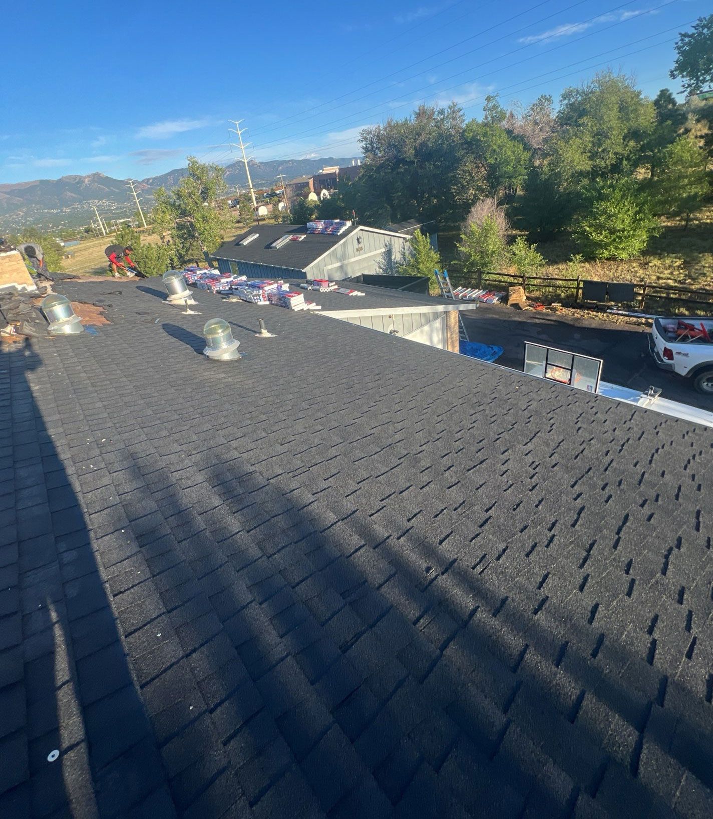 Black asphalt shingle roof with vents, overlooking a residential area with mountains and trees.