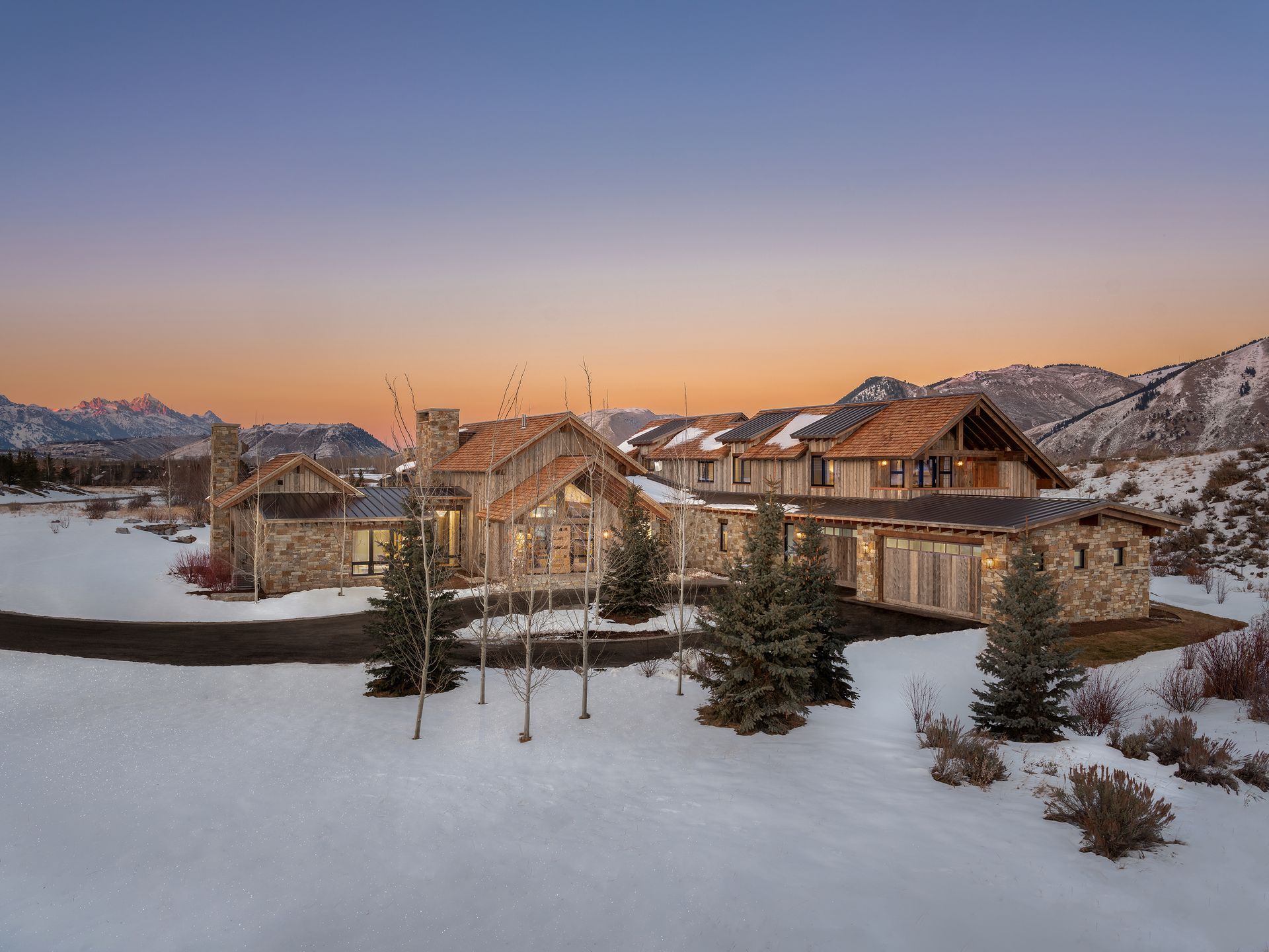 A large house in the middle of a snowy field with mountains in the background.