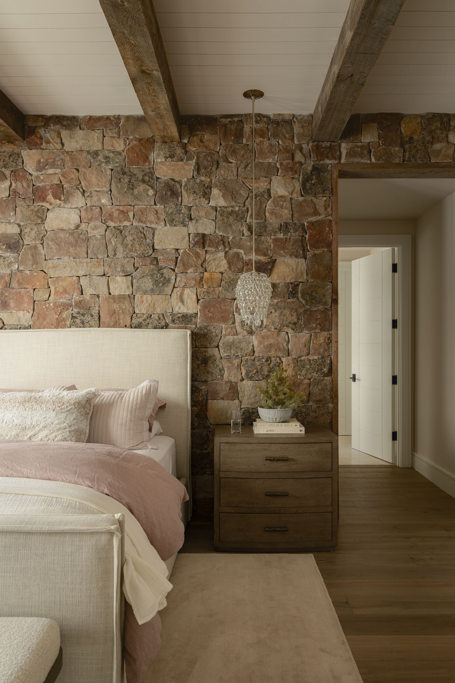 A bedroom with a bed , nightstand , and stone wall.